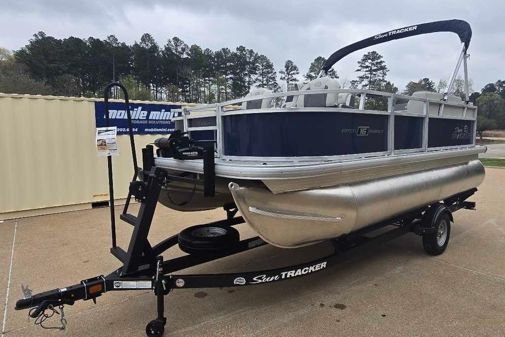 2026 Sun Tracker Bass Buggy 16 XL Select pontoon boat on trailer, parked outdoors.