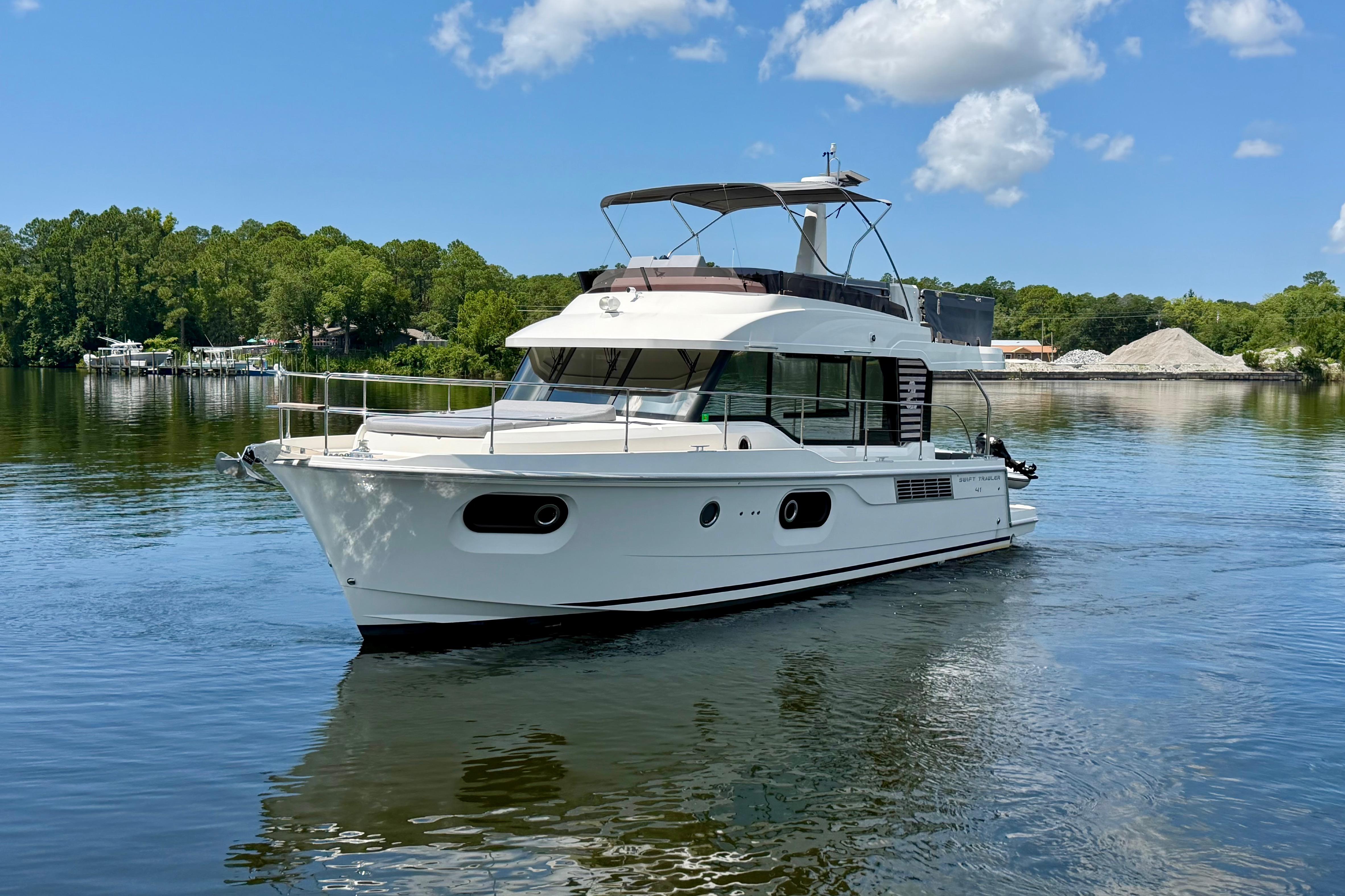 2025 Beneteau Swift Trawler 41 Fly cruising on a serene lake under a clear sky.