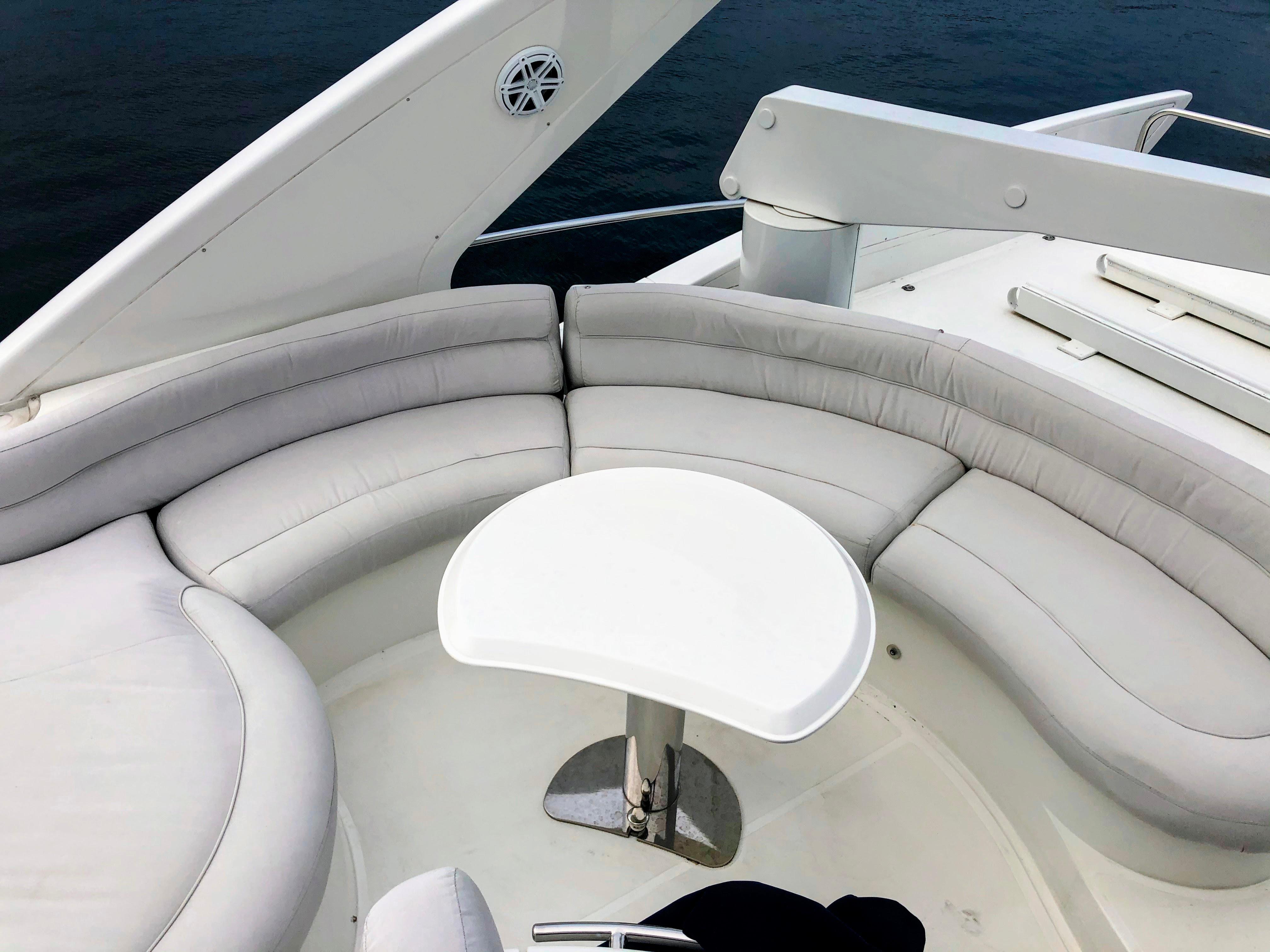 Luxurious seating area on 2002 Azimut 55 yacht, featuring white cushioned seats and table.