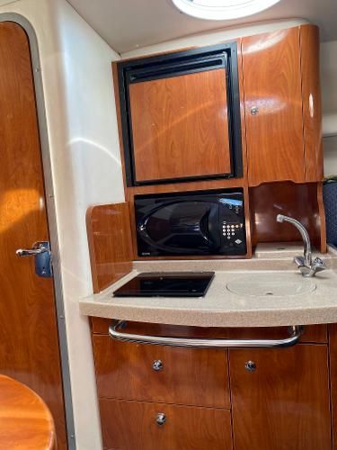 Compact boat kitchen with wooden cabinets, sink, stove, and microwave.