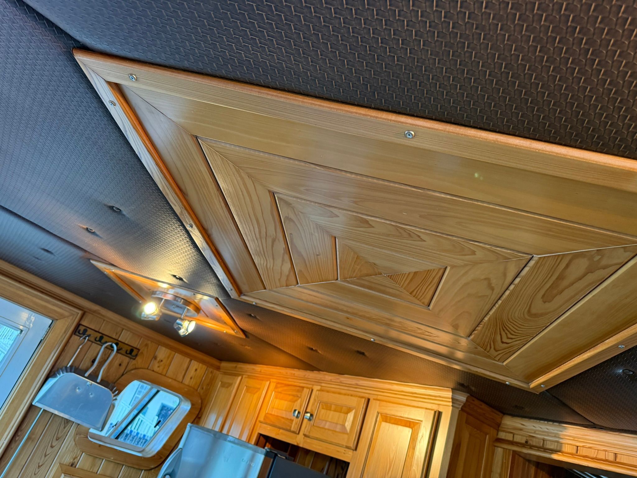 Wood-paneled ceiling in a boat with built-in lights and windows.