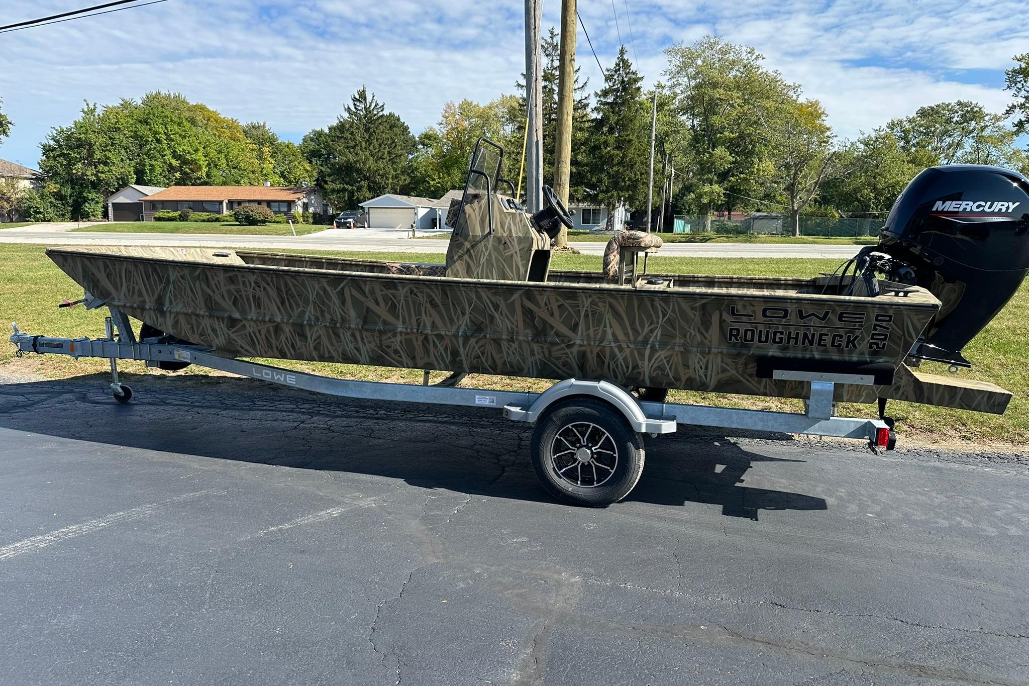 2026 Lowe Roughneck 2070CC boat on trailer, camo design, Mercury engine, parked outdoors.