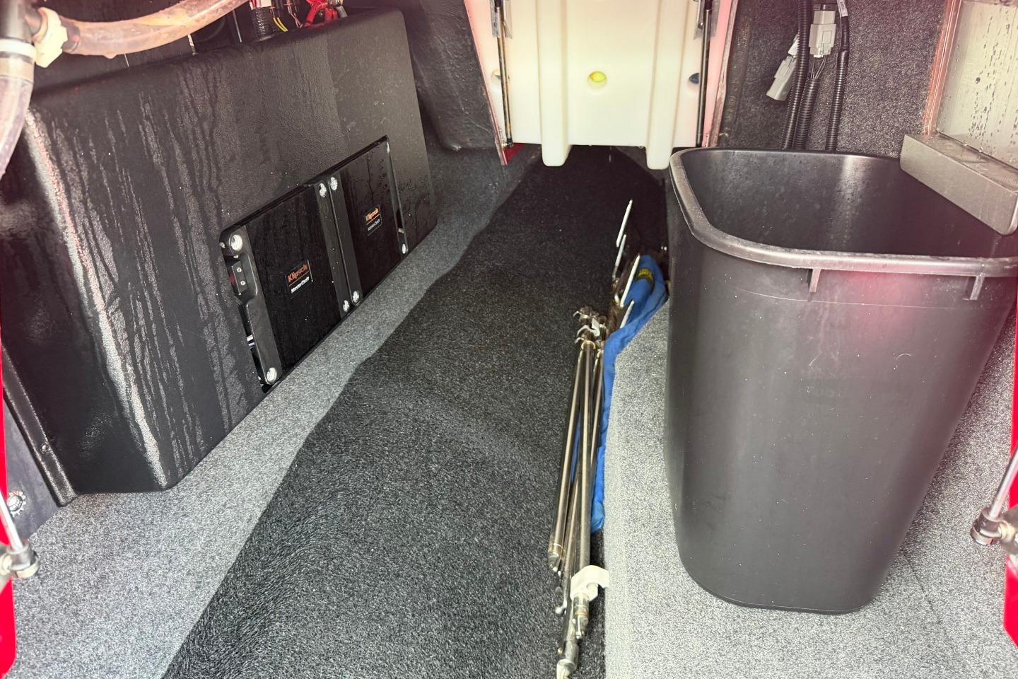 Interior storage area of a 2023 MasterCraft X24 boat with equipment and a trash bin.