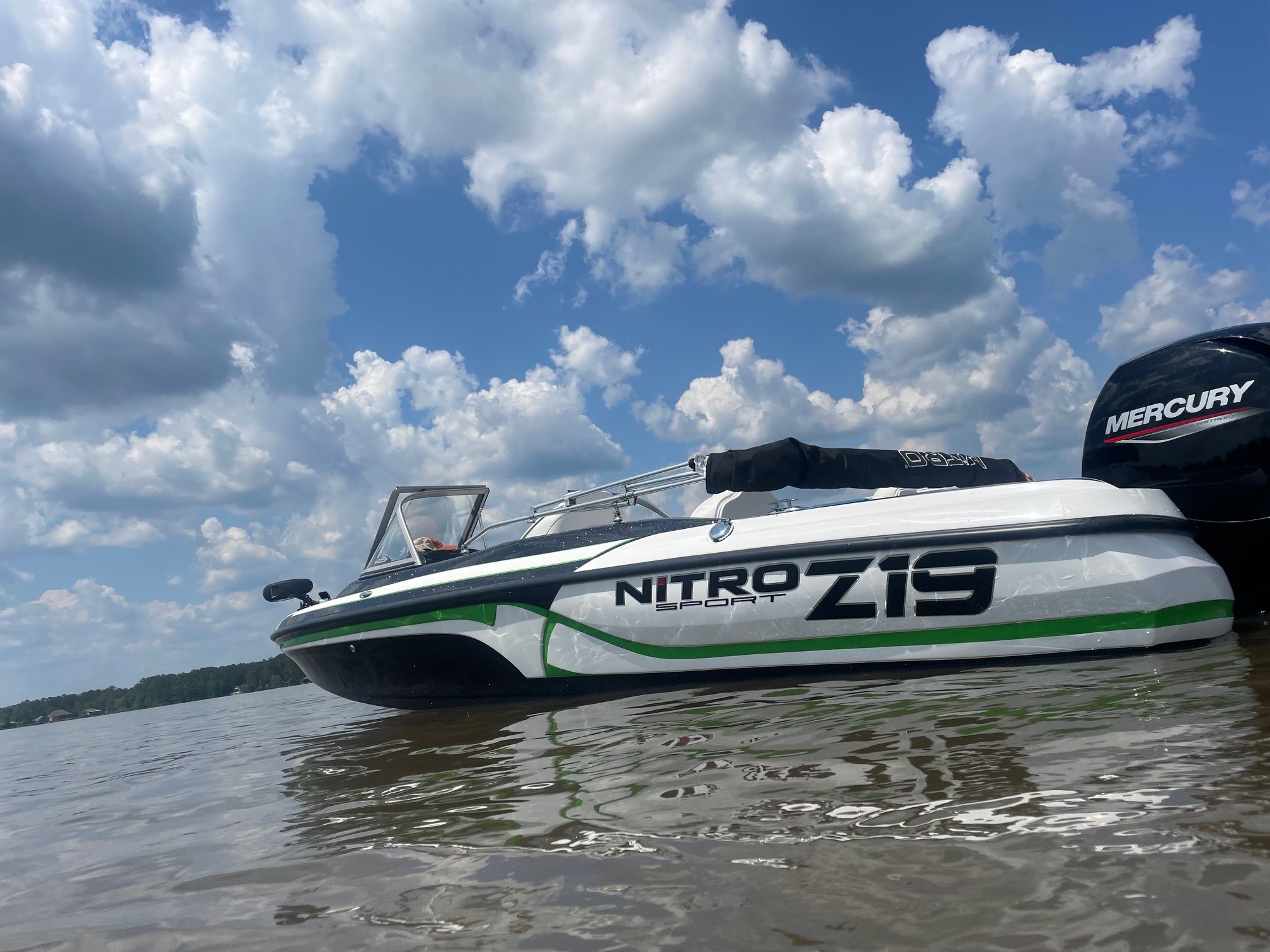 A white boat floating on calm water, featuring a Mercury engine and a blue sky.
