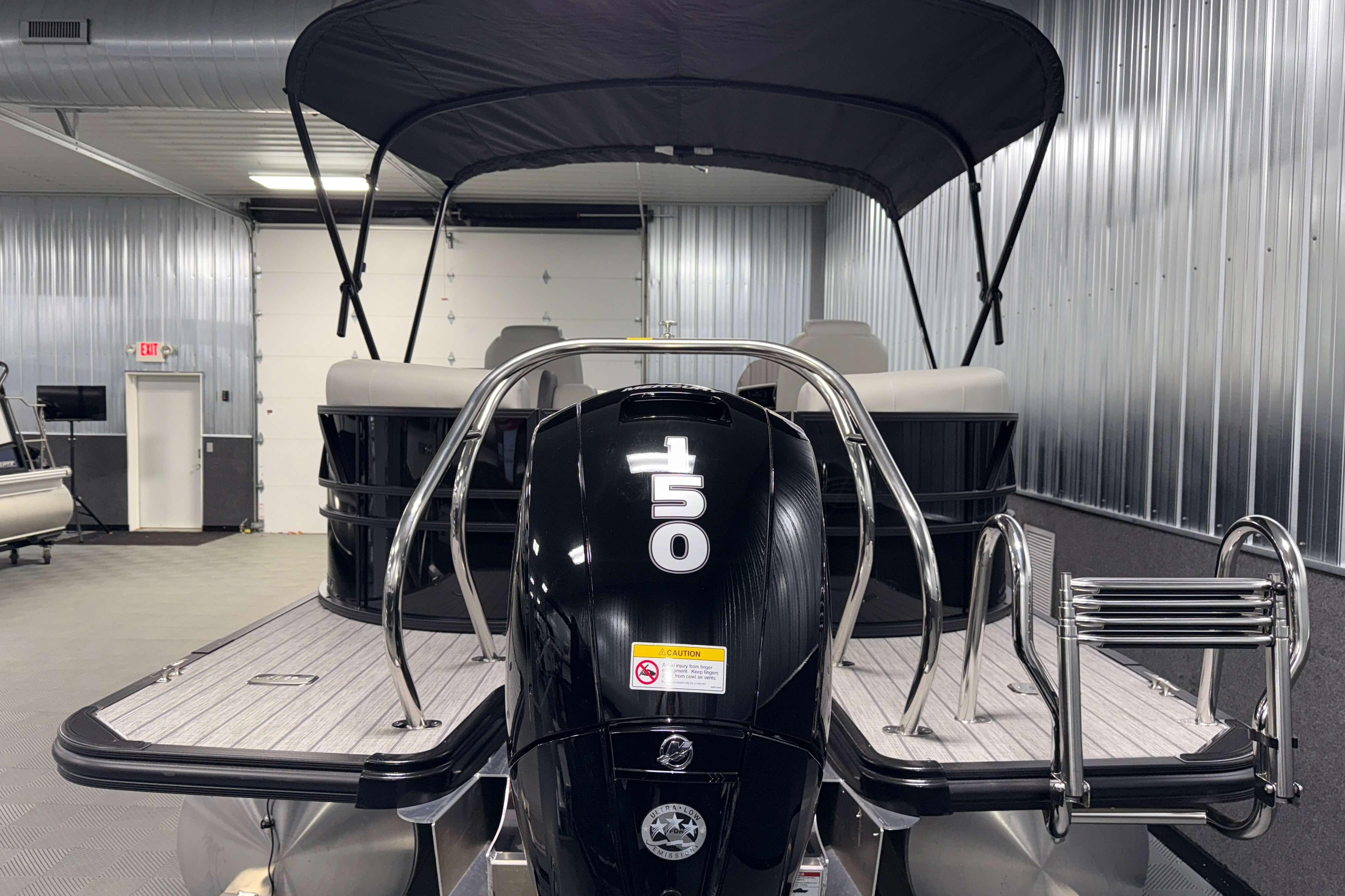 2026 Sylvan Mirage X1 pontoon boat with 150 horsepower engine in a metal-walled showroom.