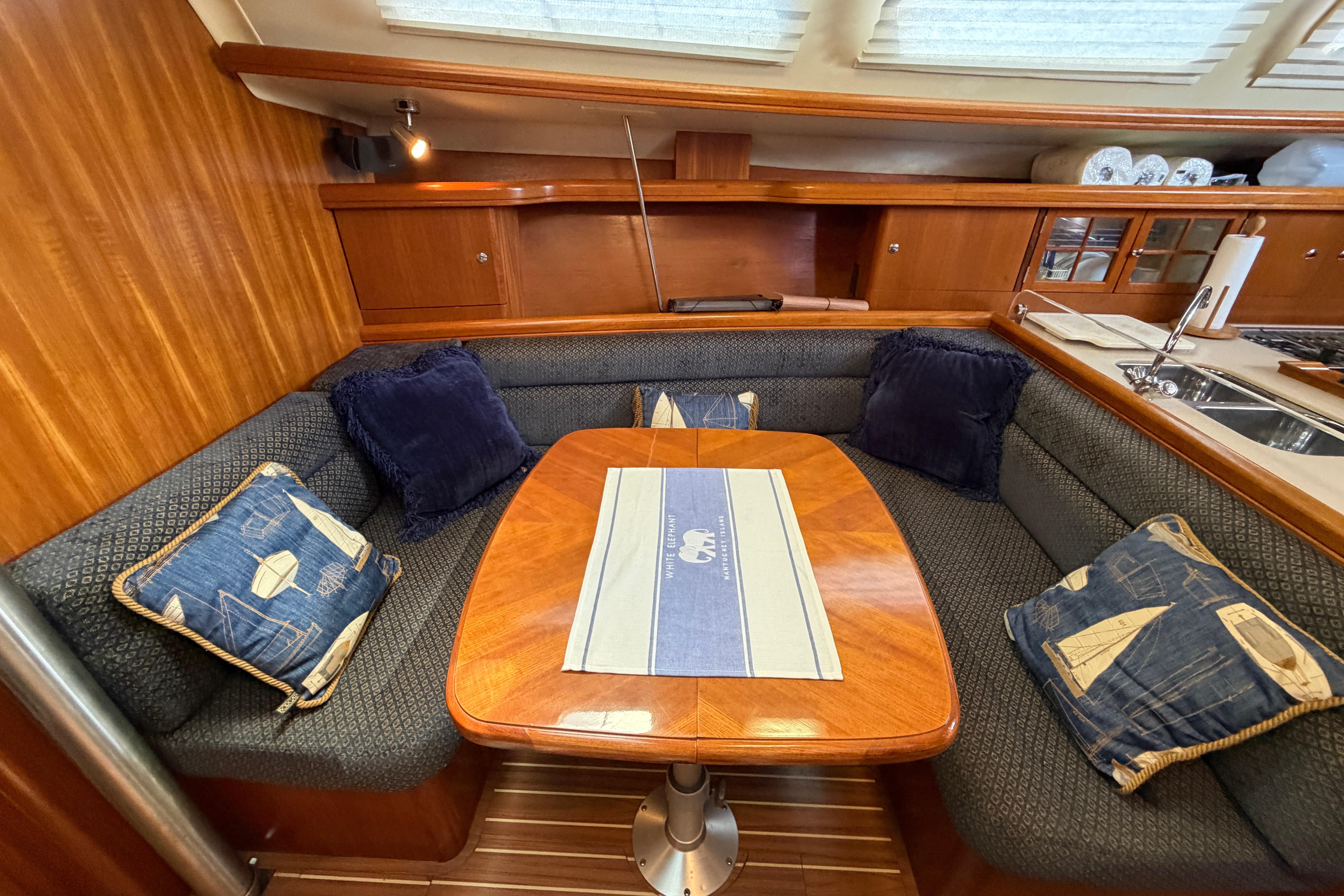 Cozy dining area in 2005 Hunter 38 sailboat with wooden table and nautical-themed cushions.