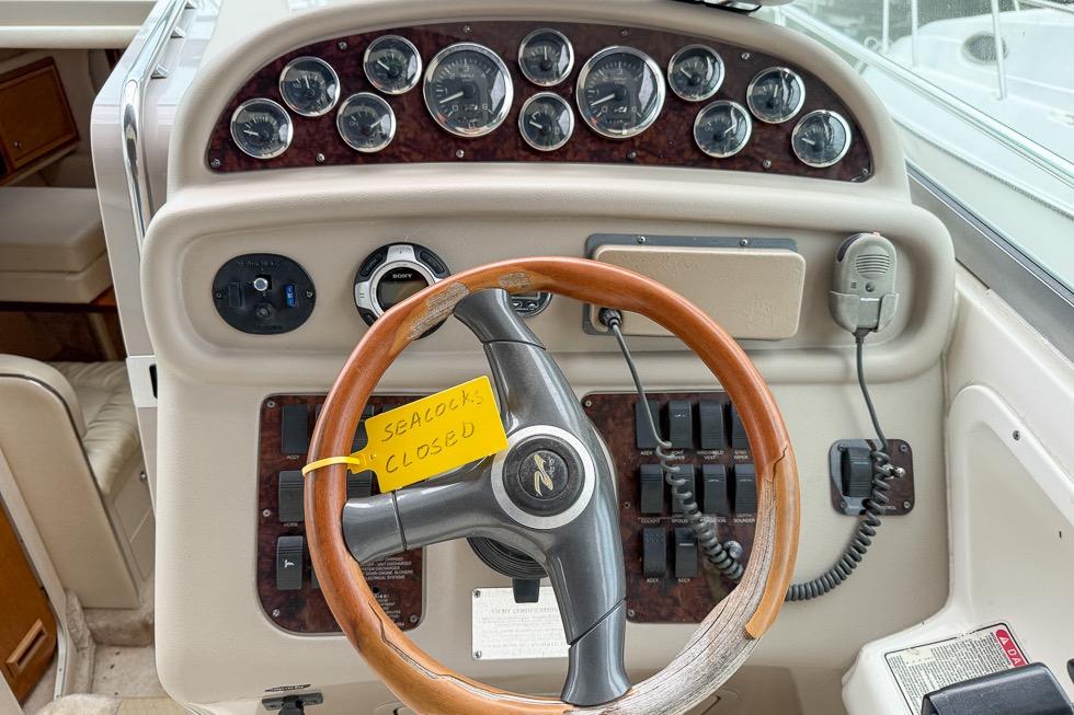 1999 Sea Ray 290 Sundancer helm with gauges, wooden steering wheel, and note reading "Seacocks Closed."