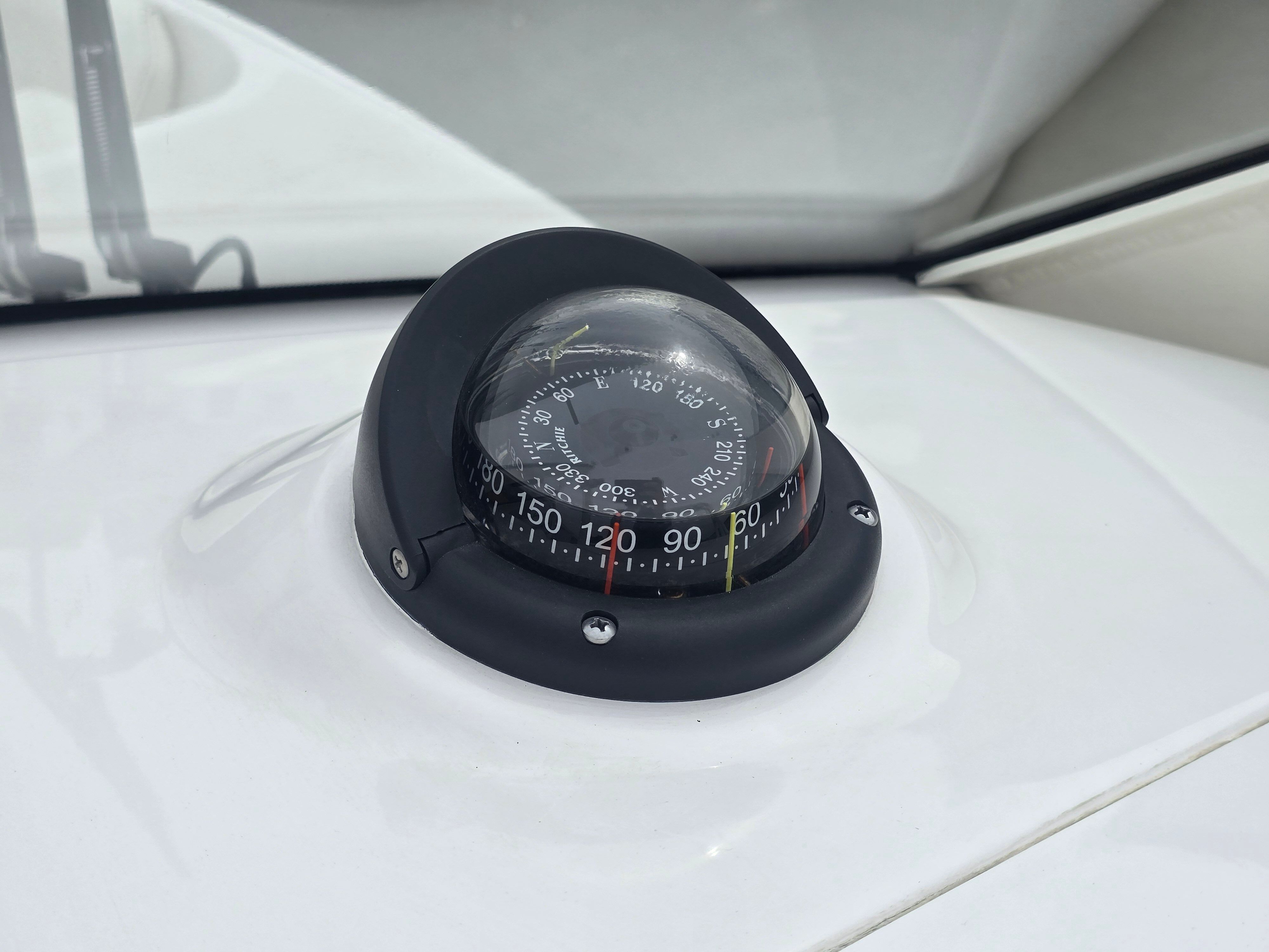 Compass on a boat's dashboard, surrounded by white material.