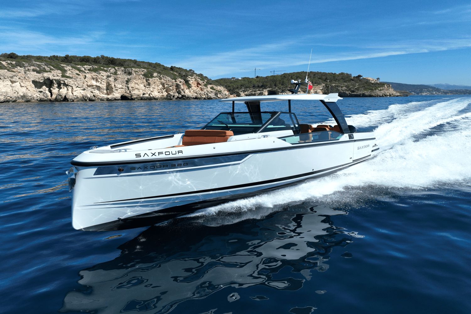 A Saxdor SX320 GTO boat speeds across blue water near a rocky coastline.