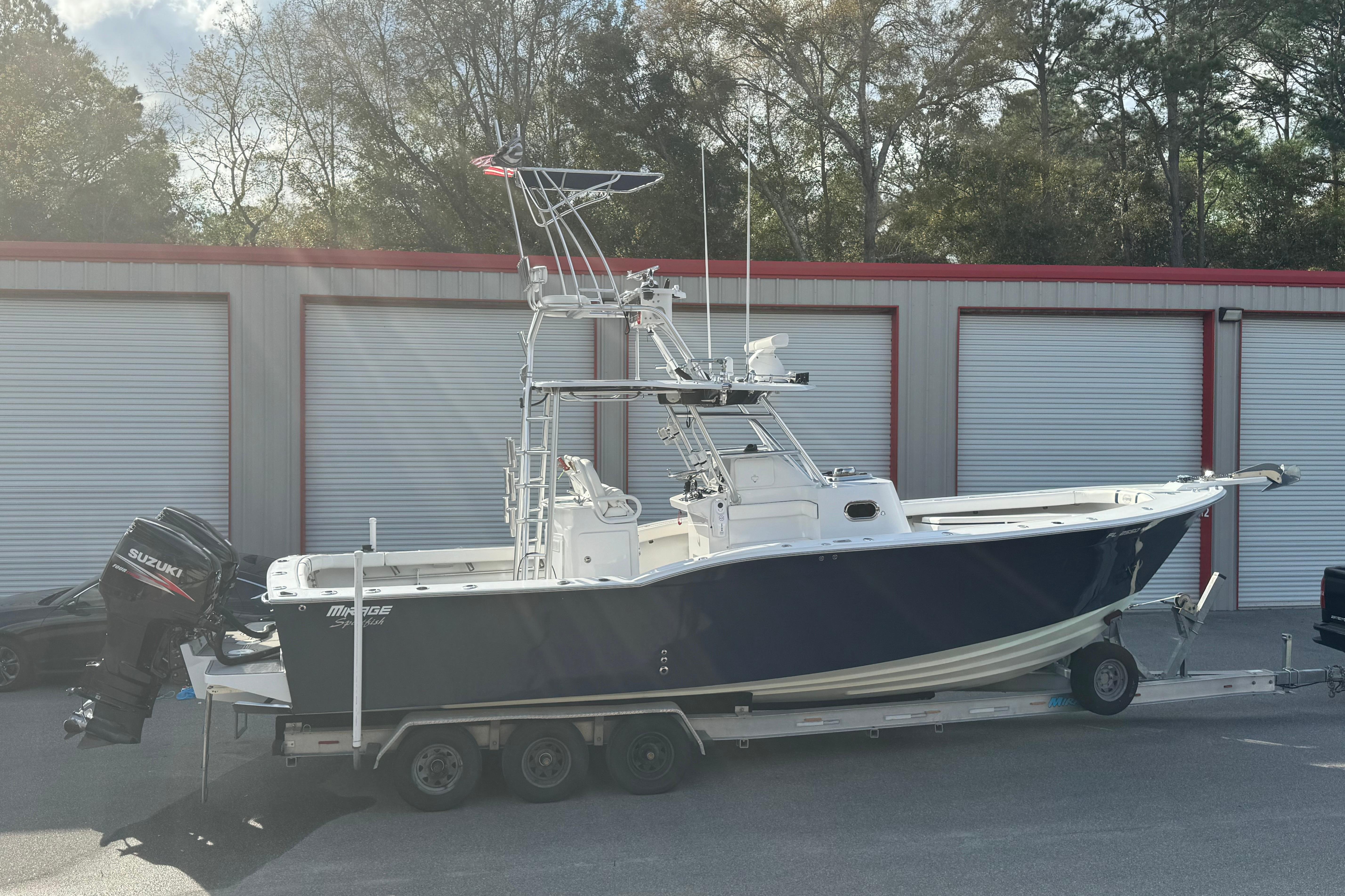 1998 Mirage Sportfish boat on trailer, parked near storage units, with Suzuki outboard motor.