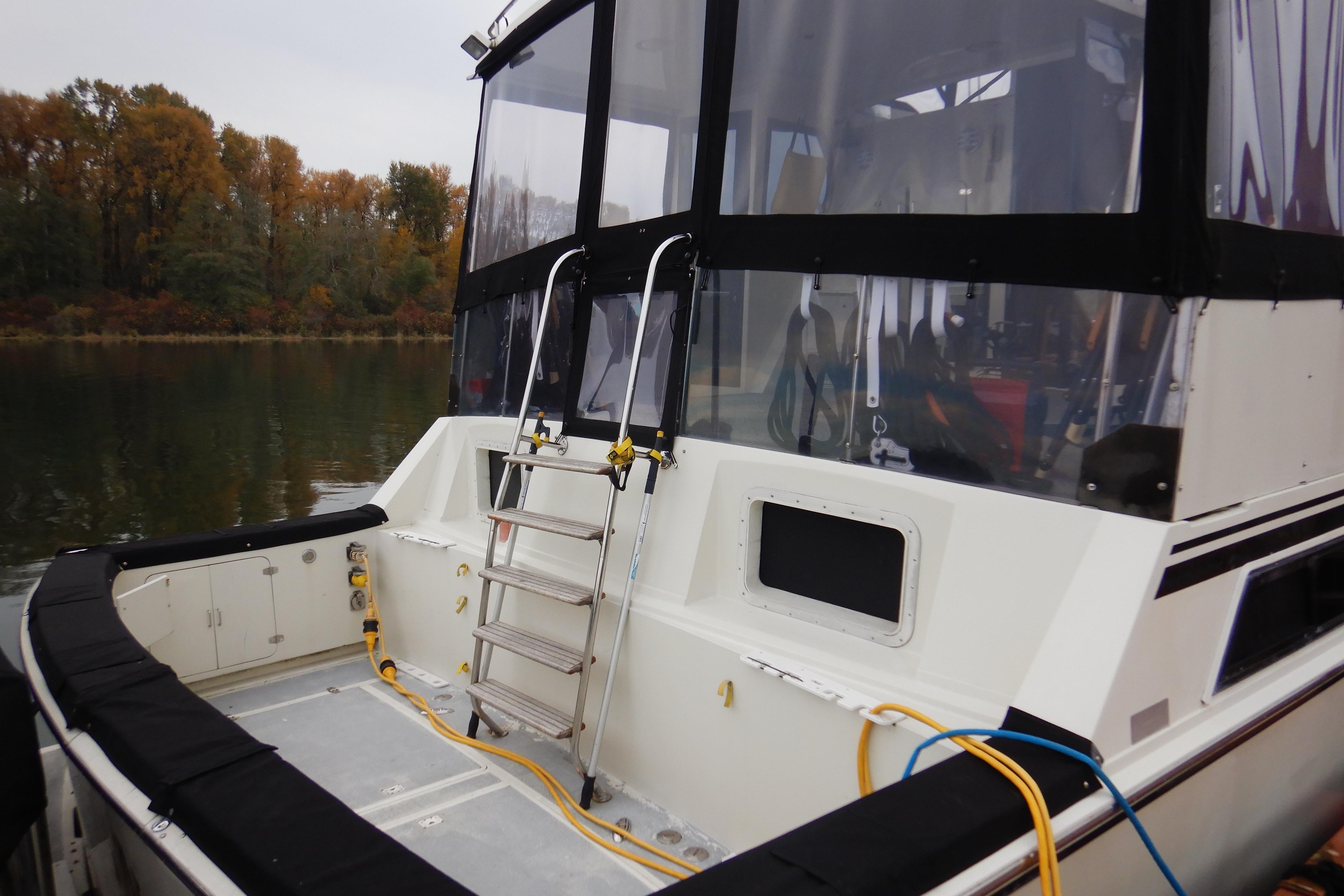 1988 Camargue 48 Cockpit Motor Yacht with ladder and cables, docked by autumn trees.