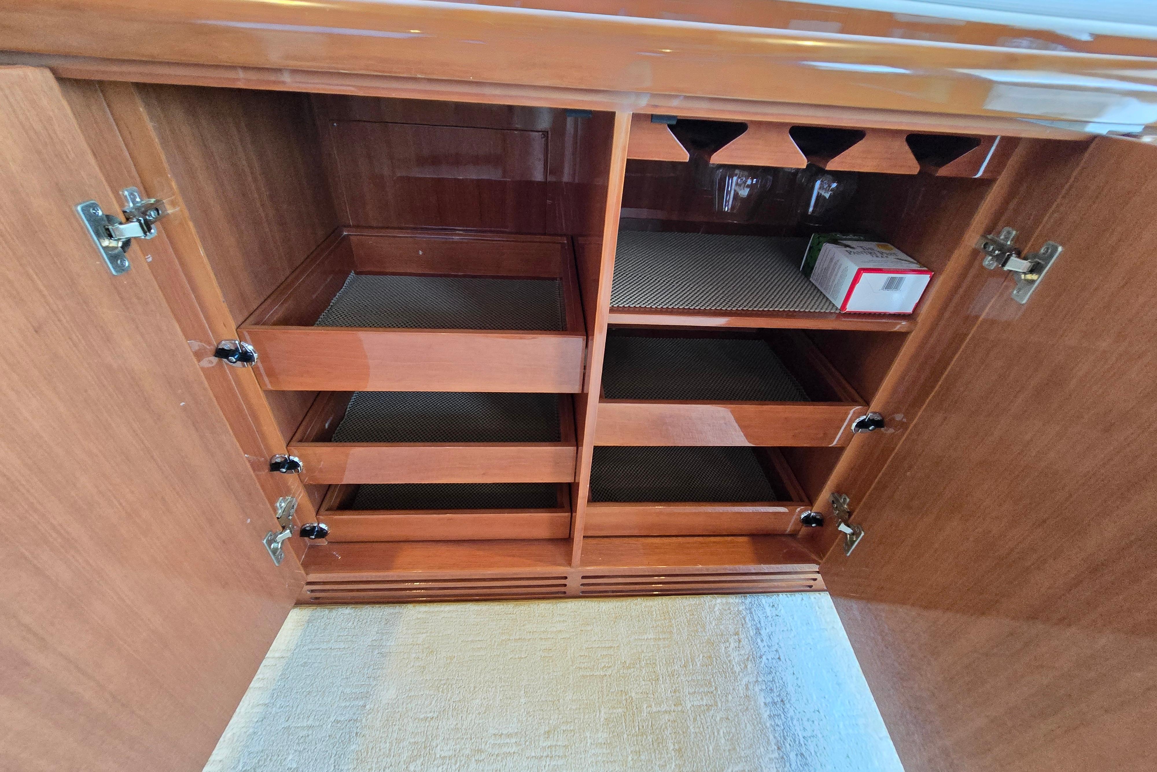 Wooden cabinet with open doors, featuring shelves and drawers, inside a 2004 Grand Harbour 58 yacht.