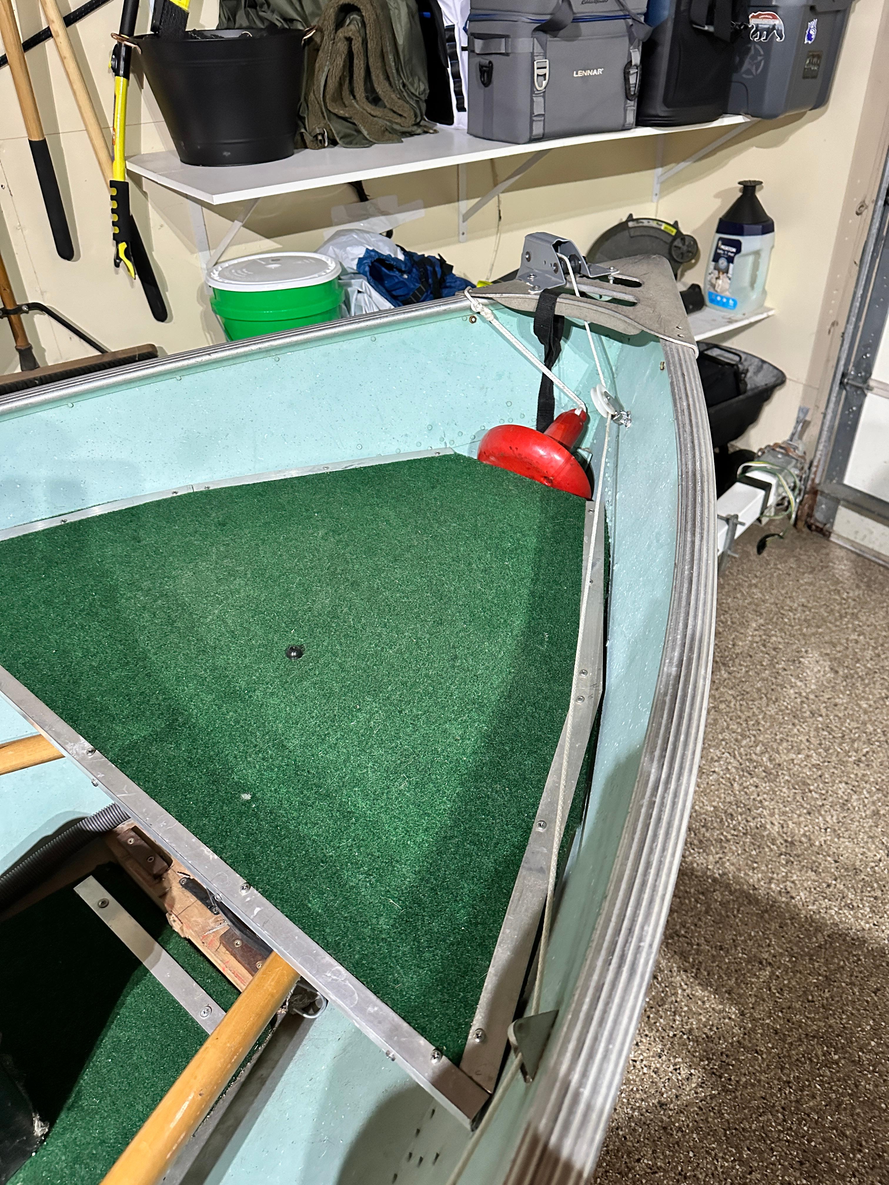 1960 Lund H boat interior with green carpet and storage shelves in a garage.