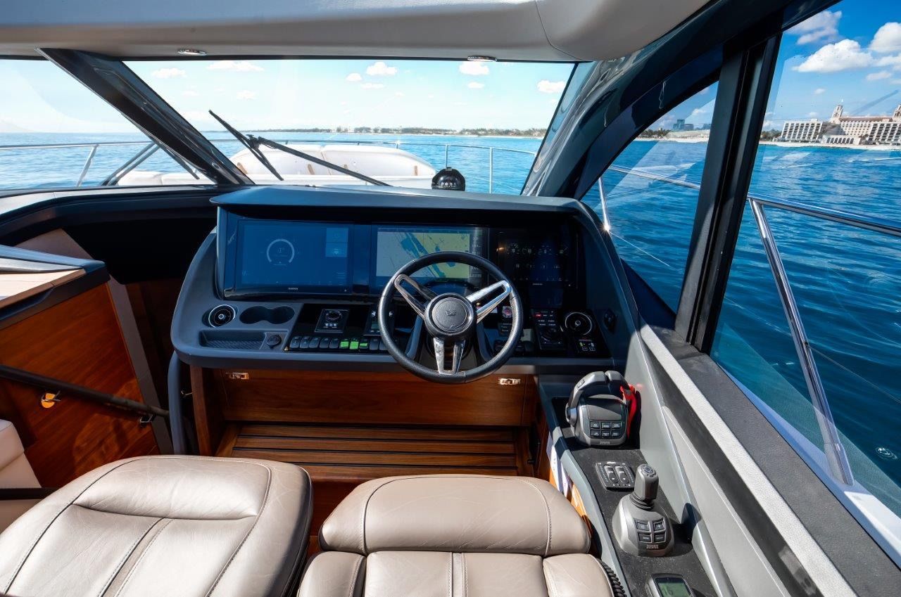 Helm of the Princess V55 yacht with modern navigation system and leather seats, surrounded by blue water.