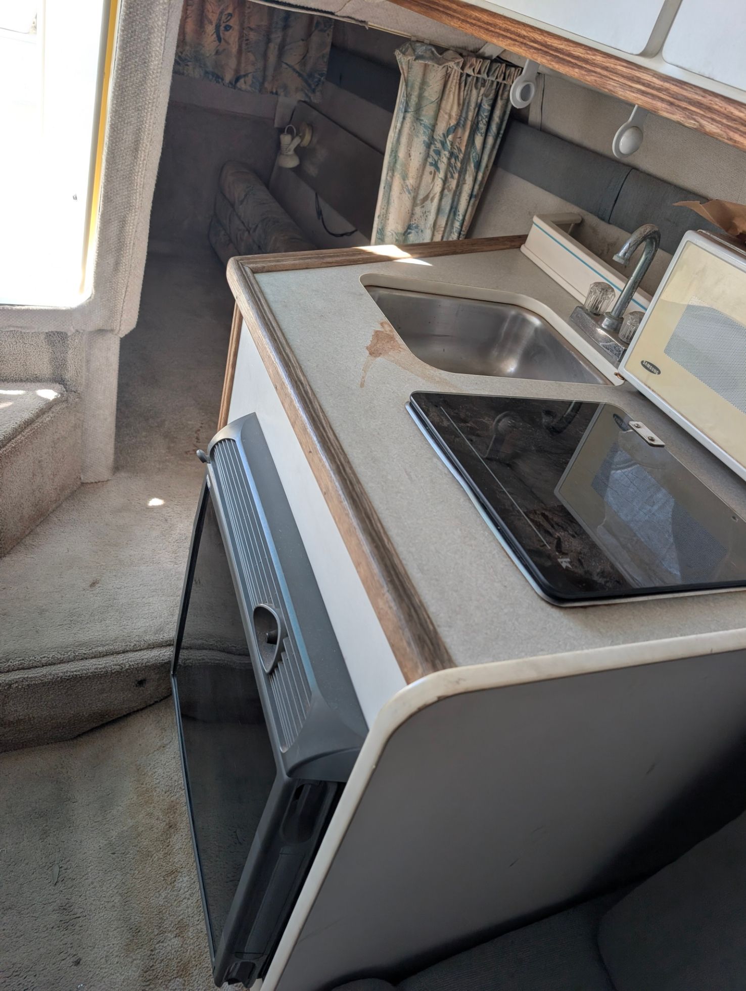 The interior of a 1995 Rinker Fiesta Vee 265 features a compact kitchen with a sink, stove, and microwave.