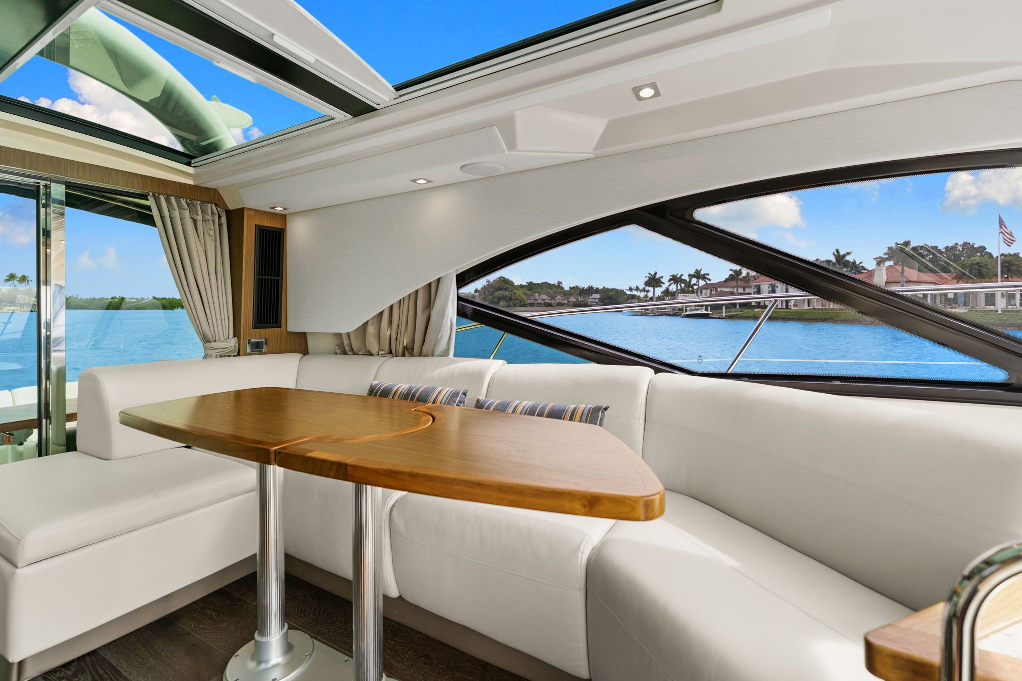 Interior of a 2017 Sea Ray Sundancer 510 with white sofa and wooden table, overlooking the water.