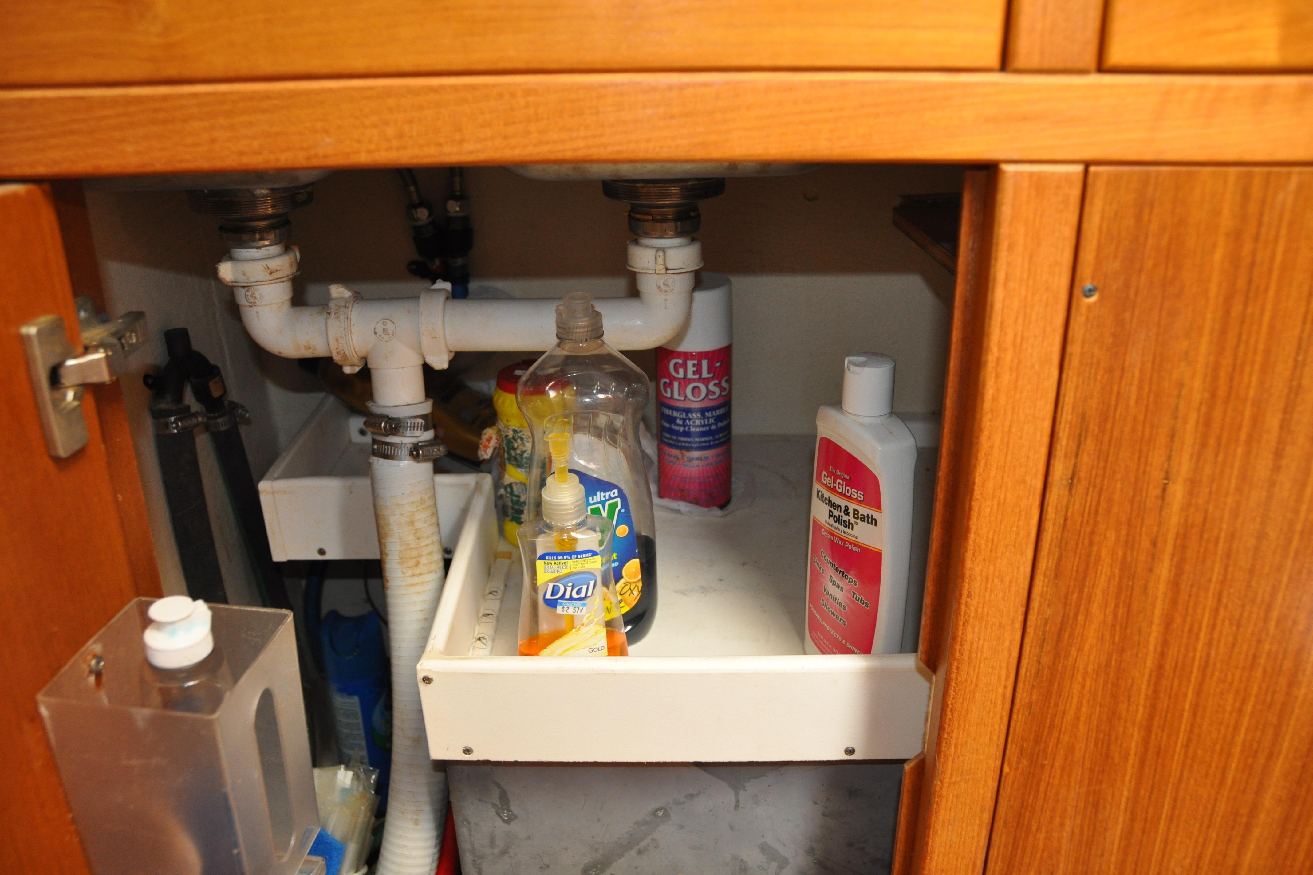Under-sink storage in a 2003 Catalina 387, featuring cleaning supplies and plumbing.