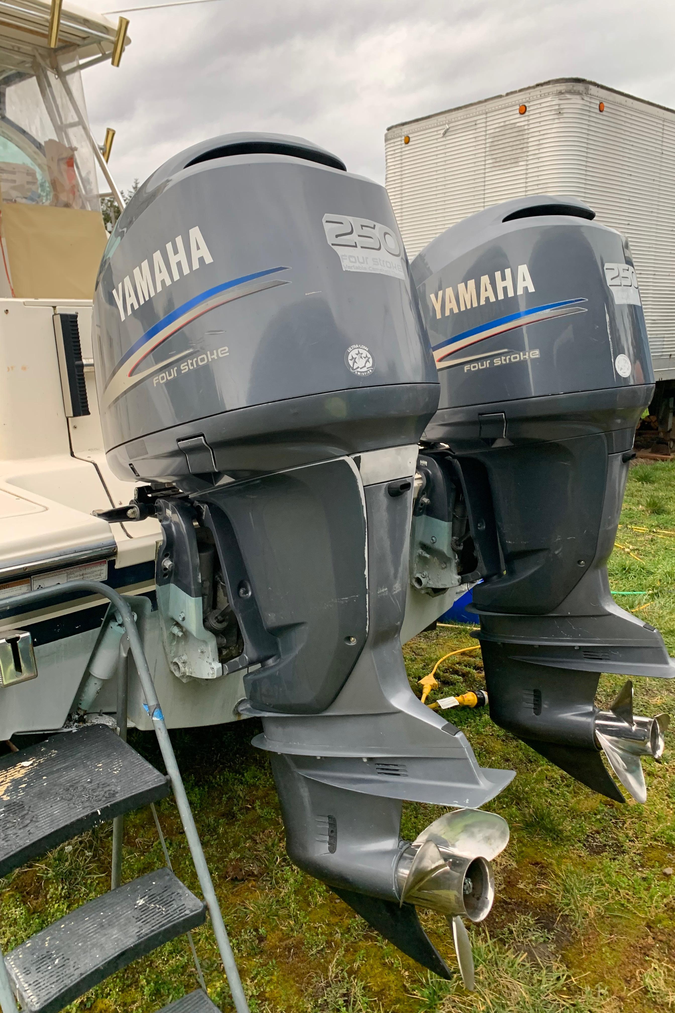 Twin Yamaha outboard motors on a 2007 Pursuit OS 335 boat, parked on grass.