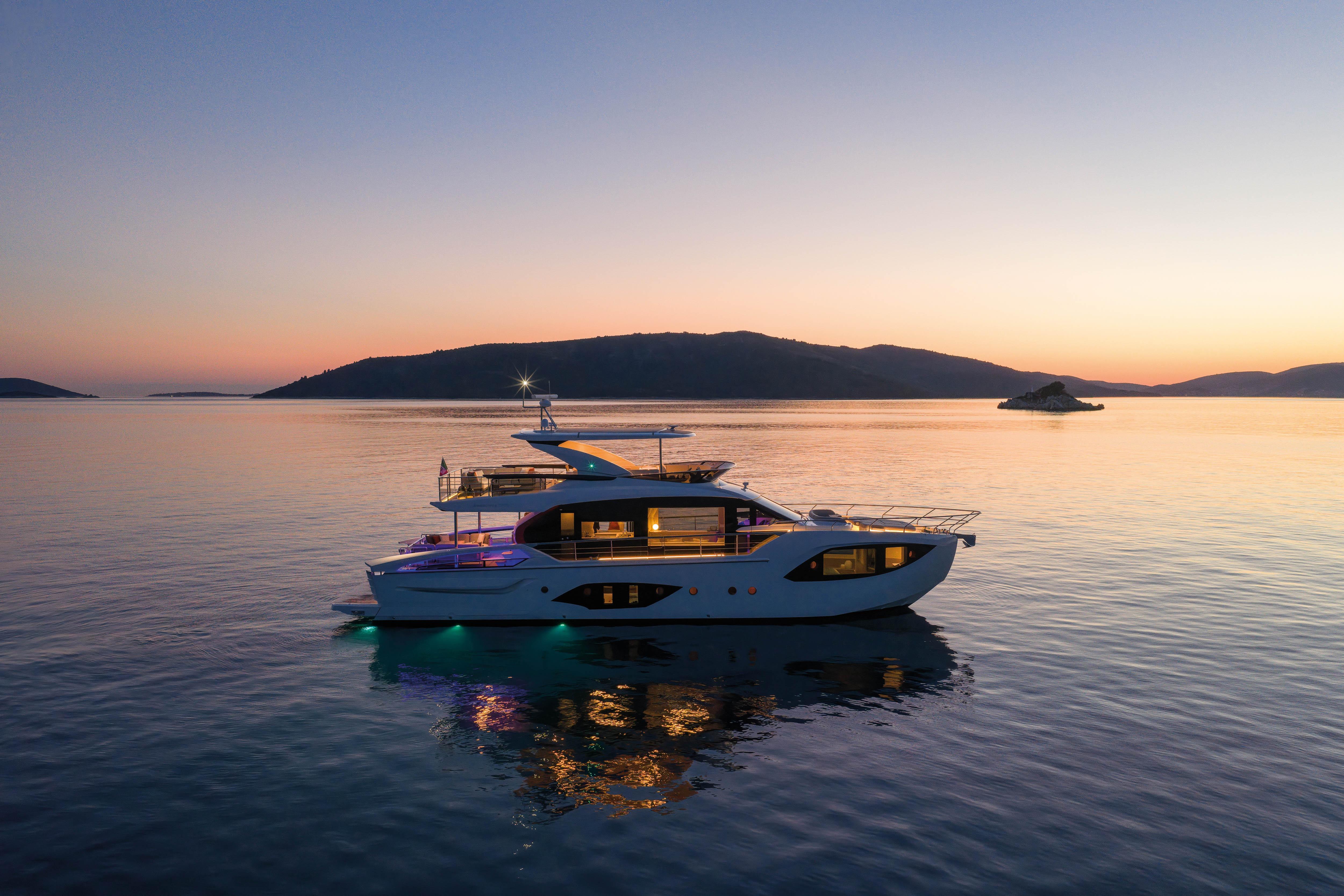 Luxury yacht at sunset on calm water, surrounded by hills.