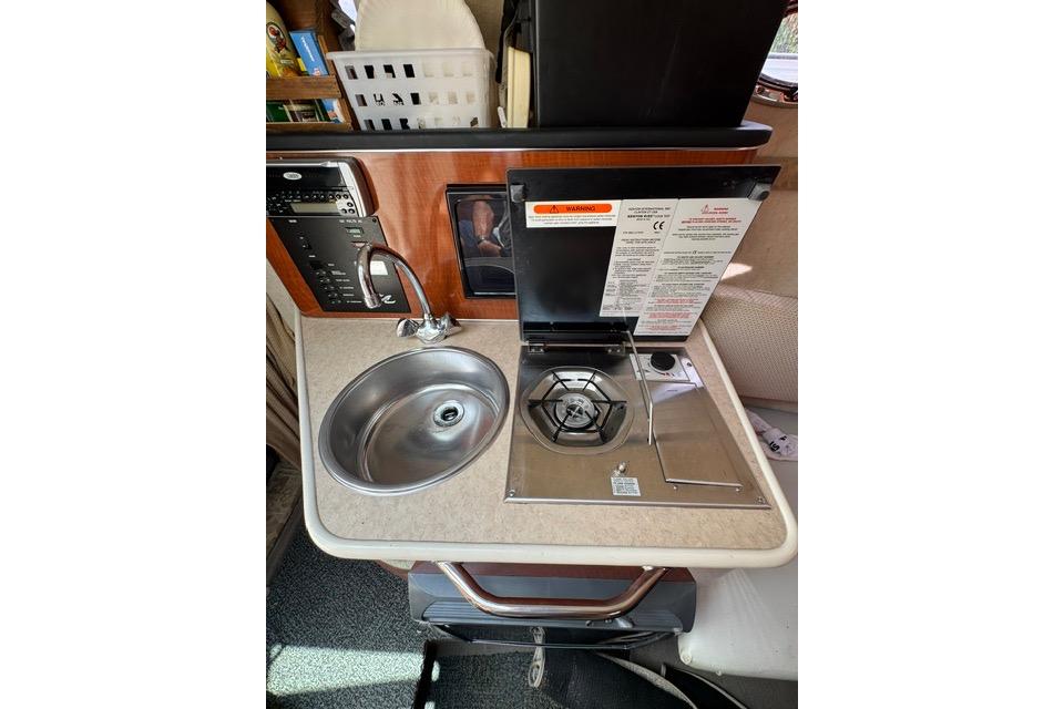 Compact kitchenette in a 2004 Sea Ray 240 Sundancer boat with sink and stove.