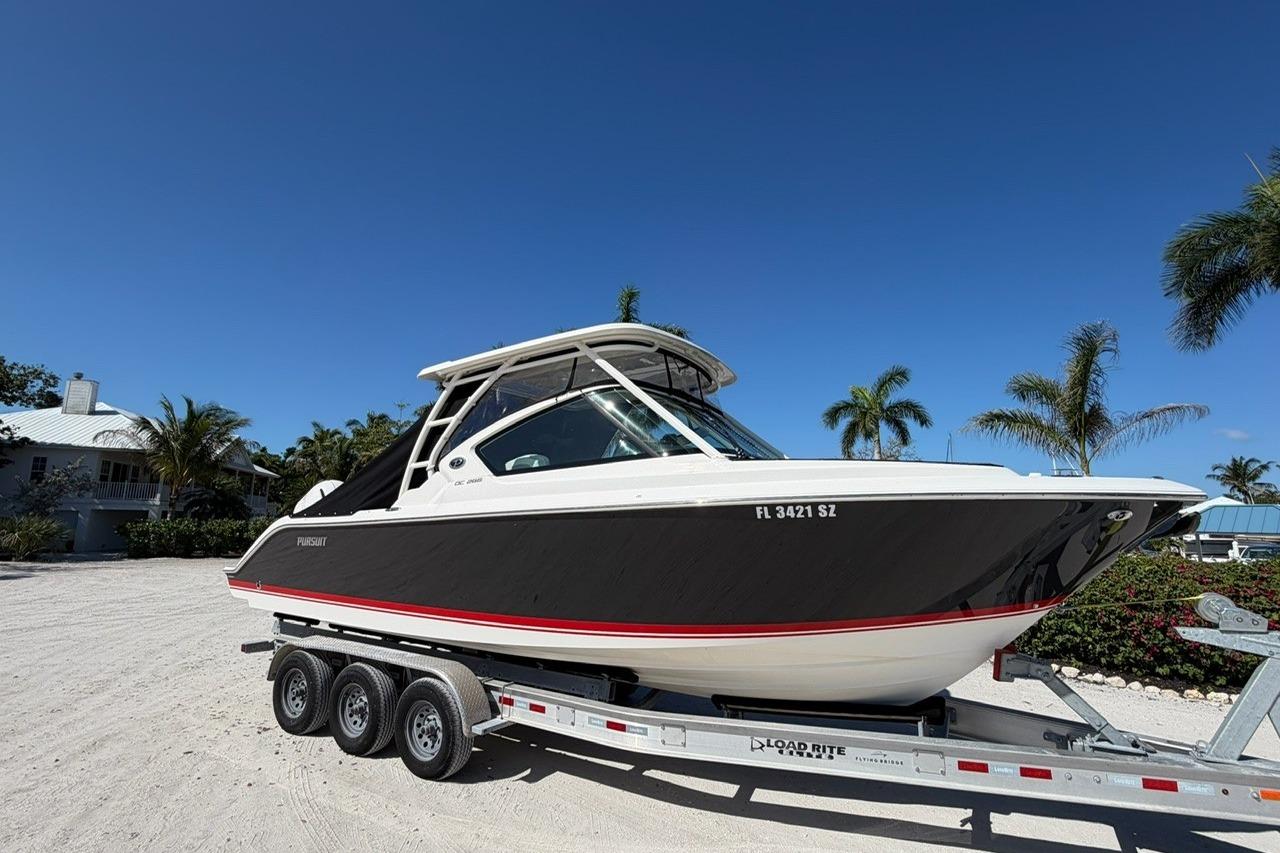 2021 Pursuit DC 266 Dual Console boat on trailer, sunny day, palm trees background.