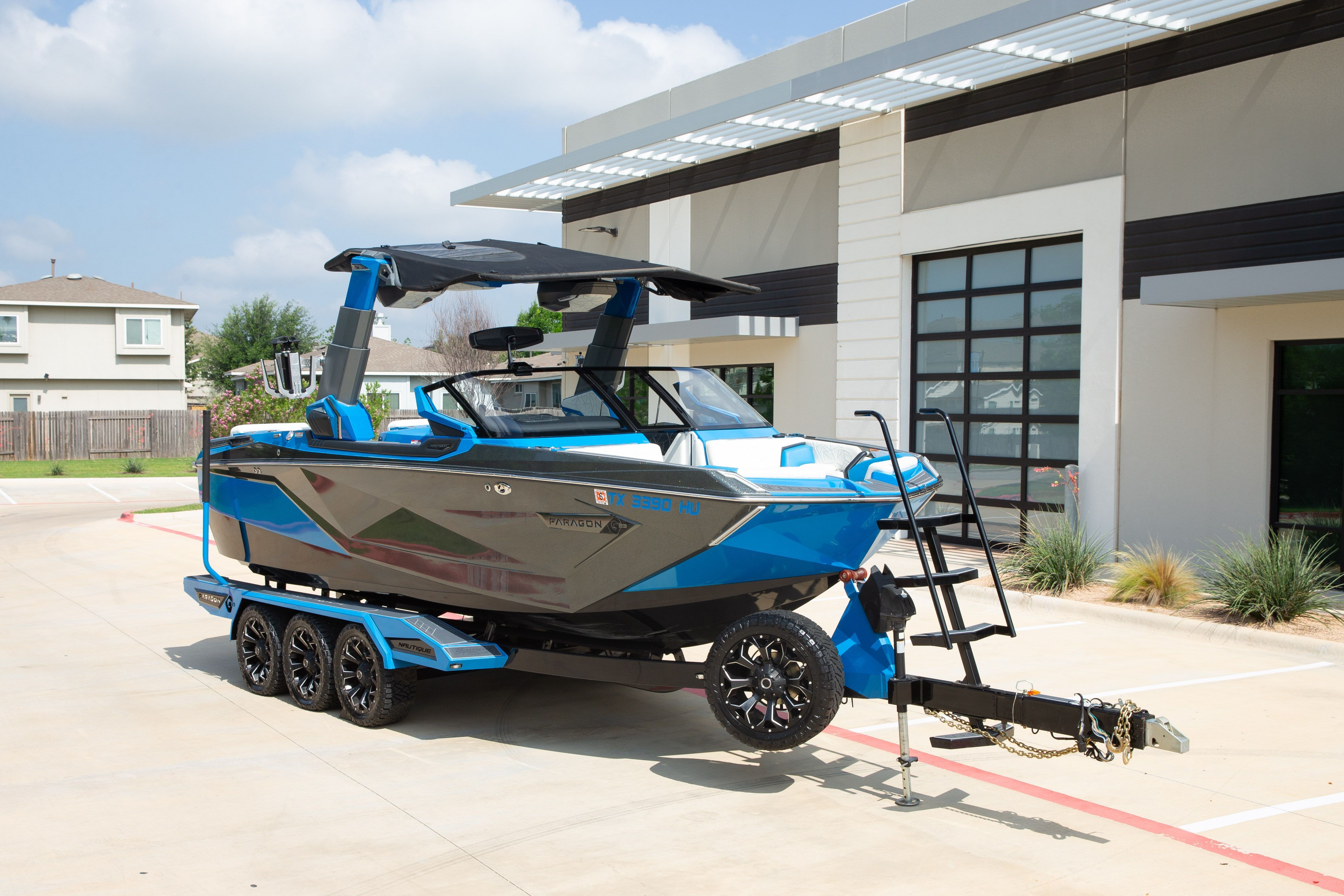 A blue and gray boat on a trailer in front of a modern building.