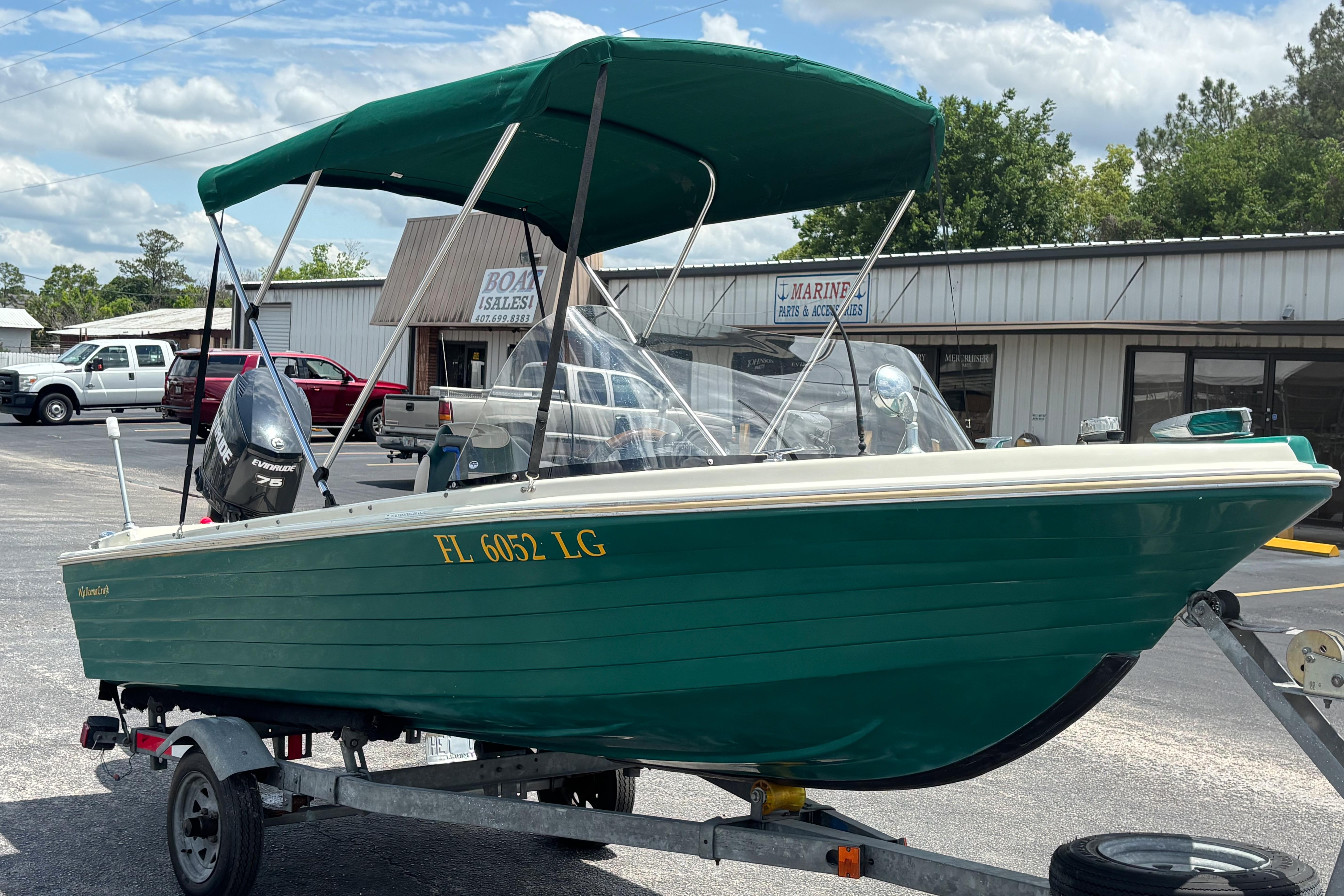 1966 Mohawk 15 boat with green hull on trailer, parked outside marine store.