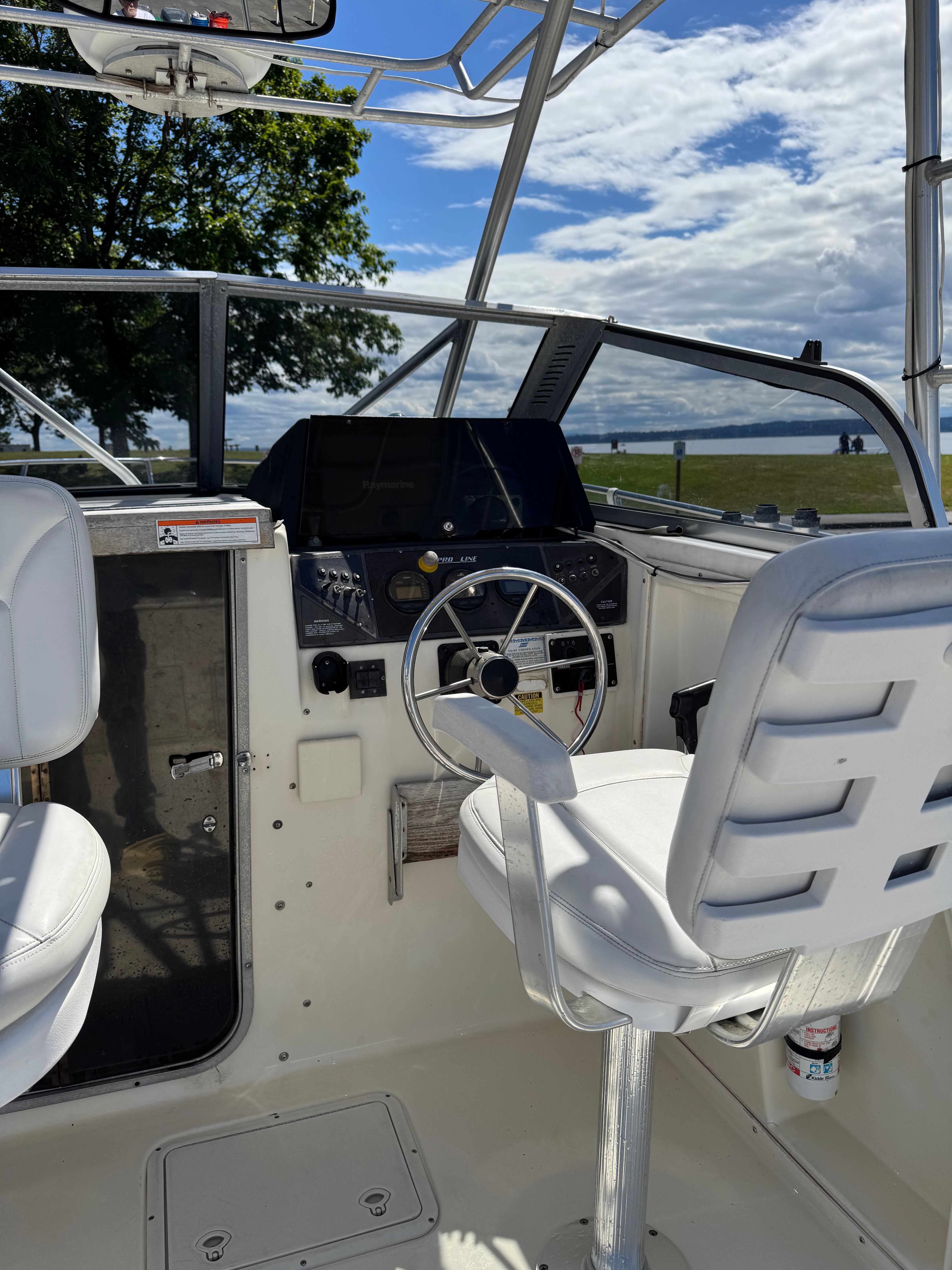 Interior view of a boat with white seats and steering wheel, surrounded by trees and water.