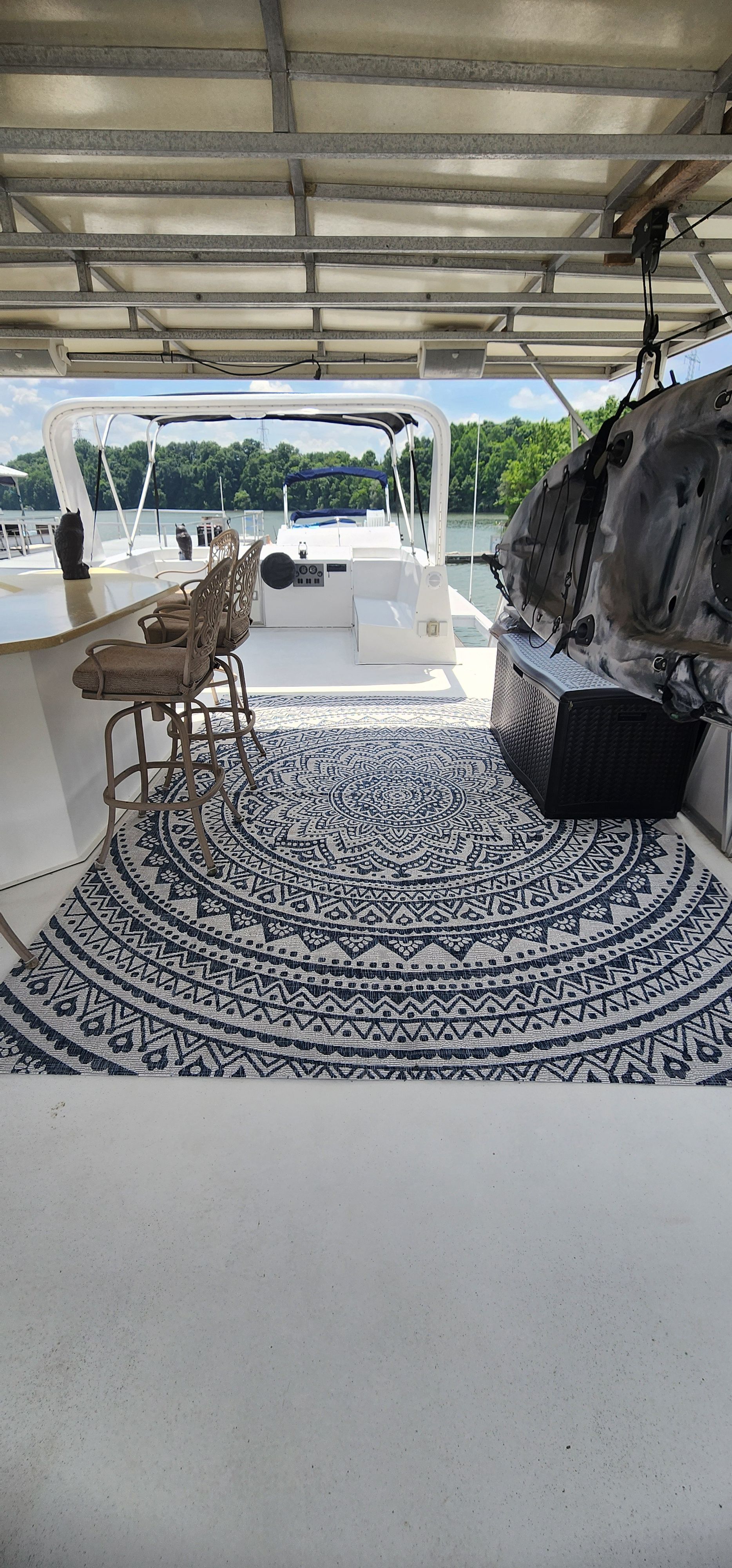 The boat features a covered deck with a patterned rug and bar stools.