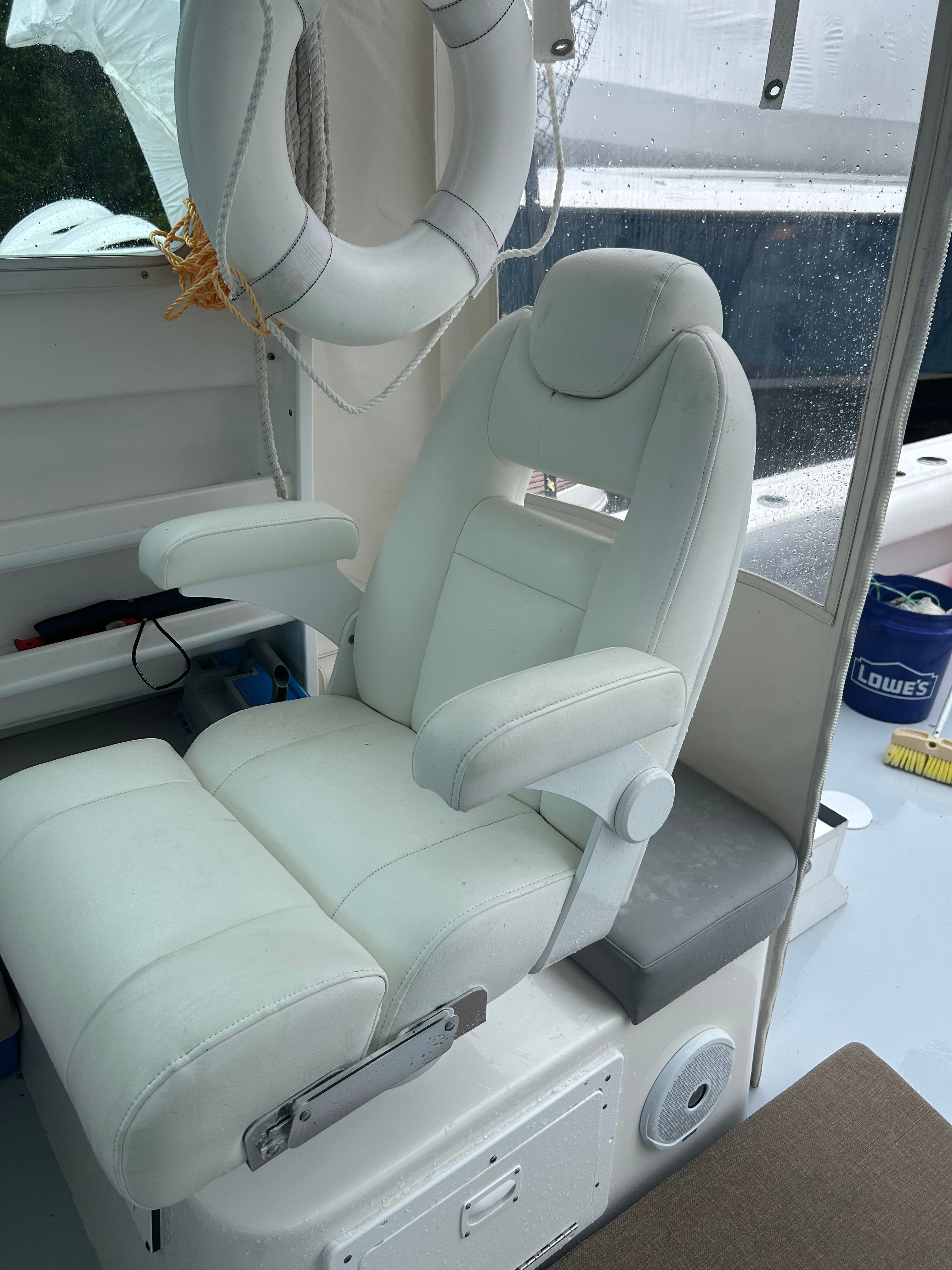 White captain's chair with armrests on a boat, surrounded by wet surfaces.