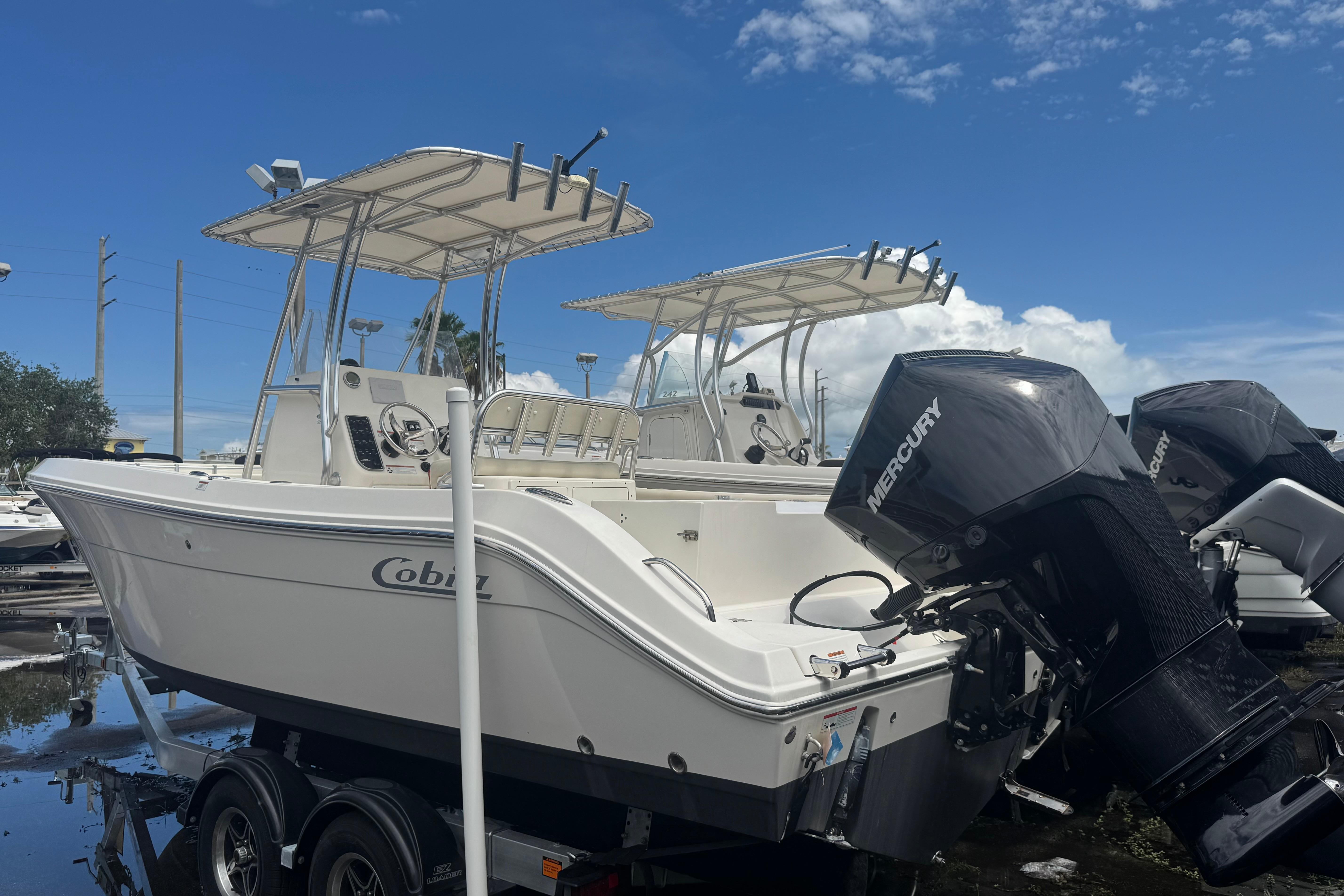 2022 Cobia 237 Center Console boat with Mercury engines, parked on a trailer under a clear blue sky.