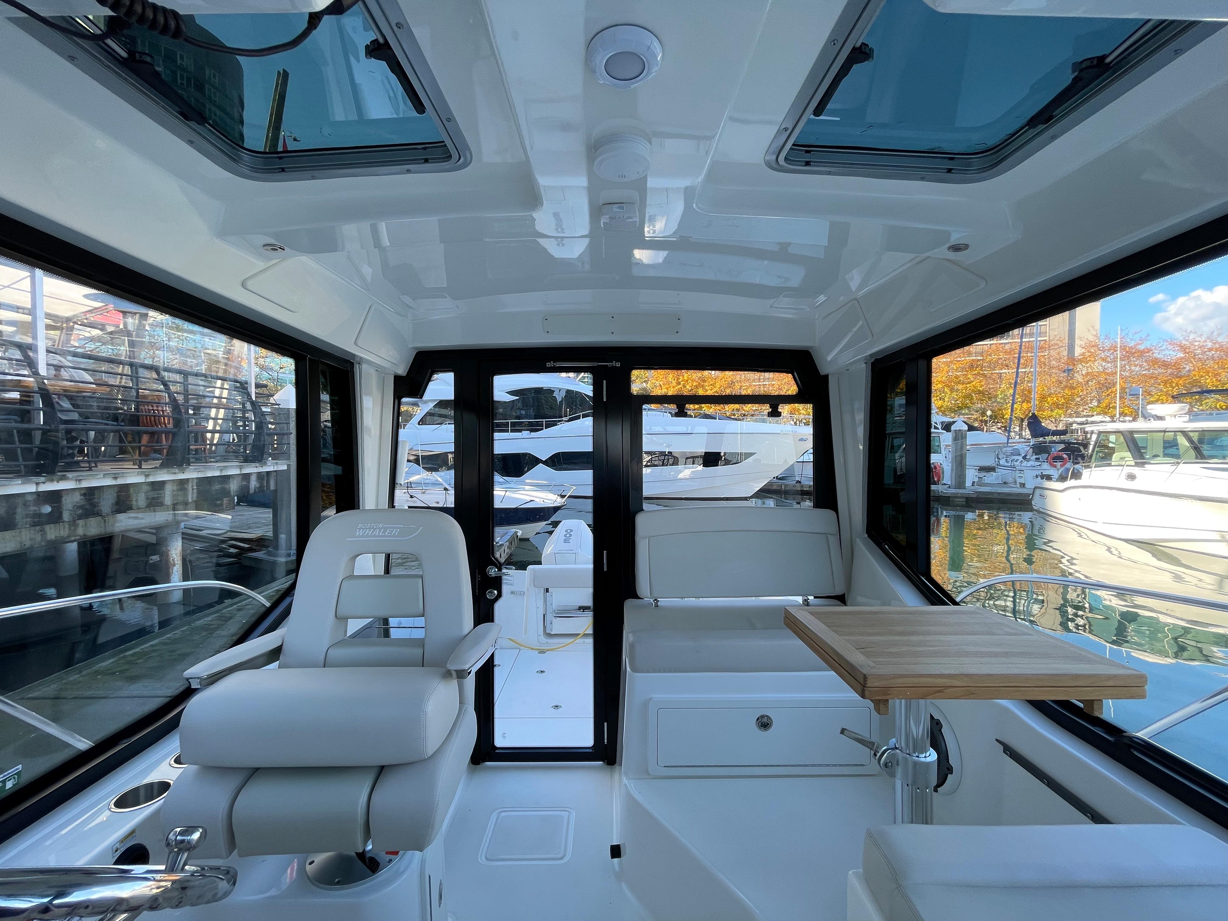2025 Boston Whaler 325 Conquest Pilothouse interior with seating and table, docked at marina.