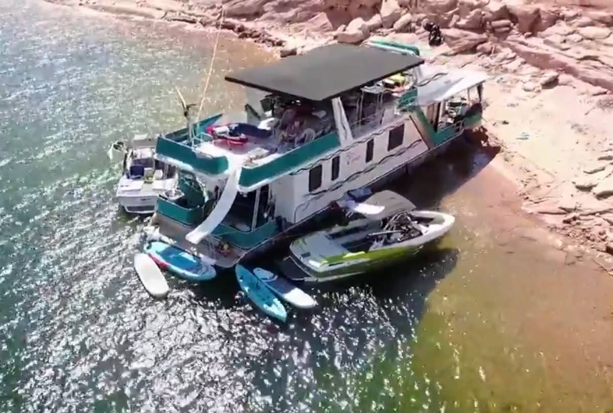 1993 Lakeview houseboat docked by rocky shore with jet ski and paddleboards.