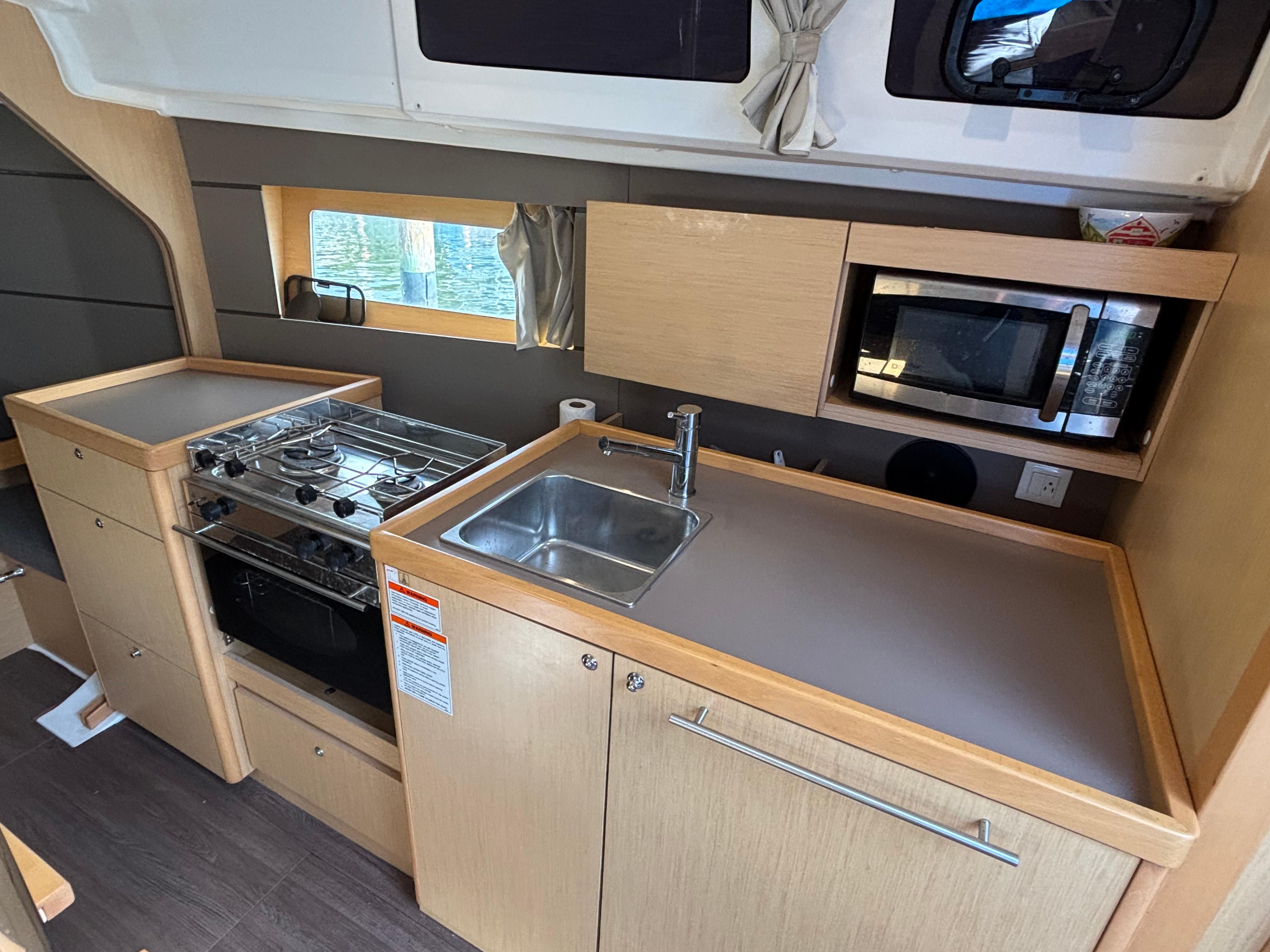 Modern kitchen in 2015 Beneteau Oceanis 35 yacht with stove, sink, and microwave.
