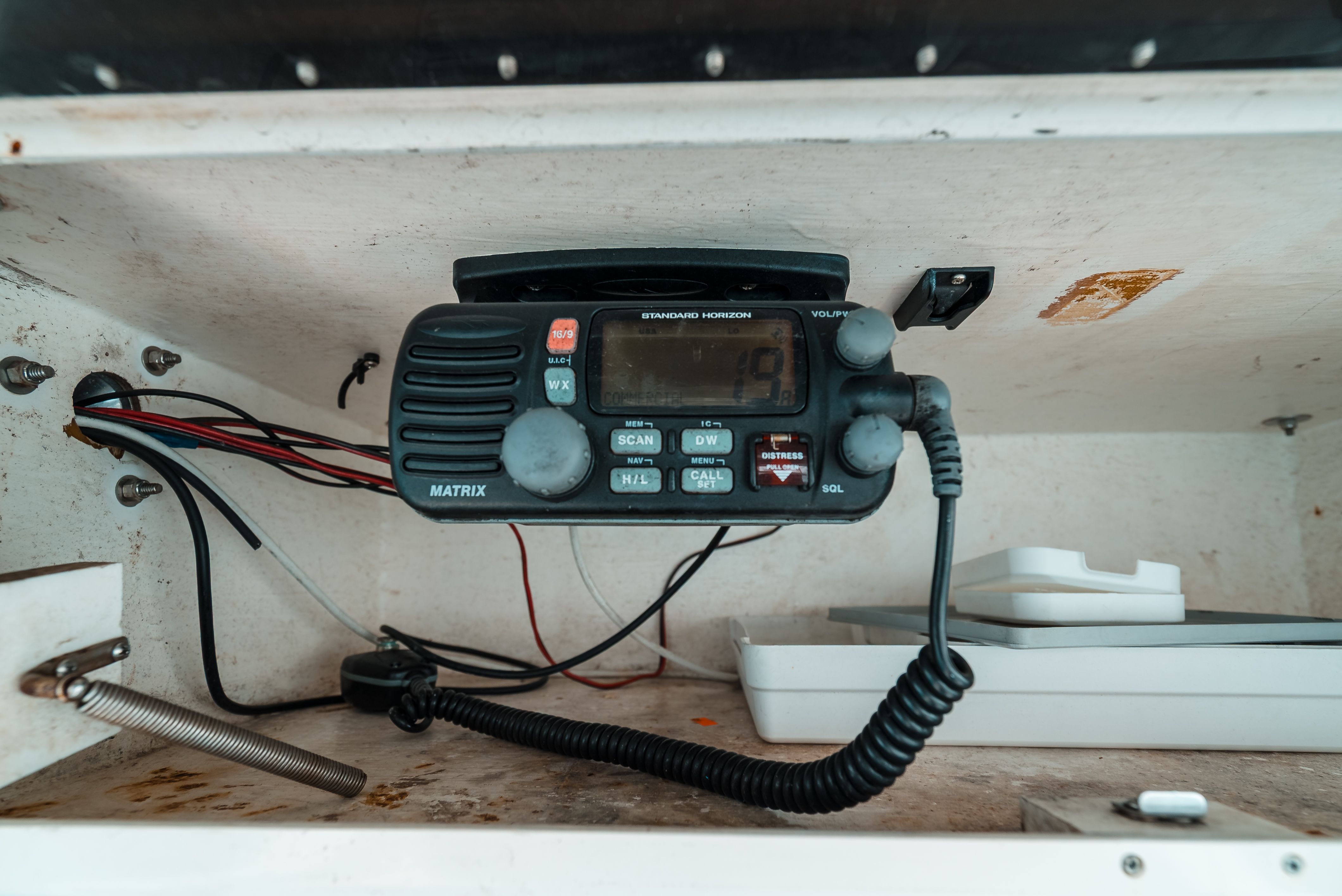 A radio in a boat cabinet, surrounded by wires and storage compartments.