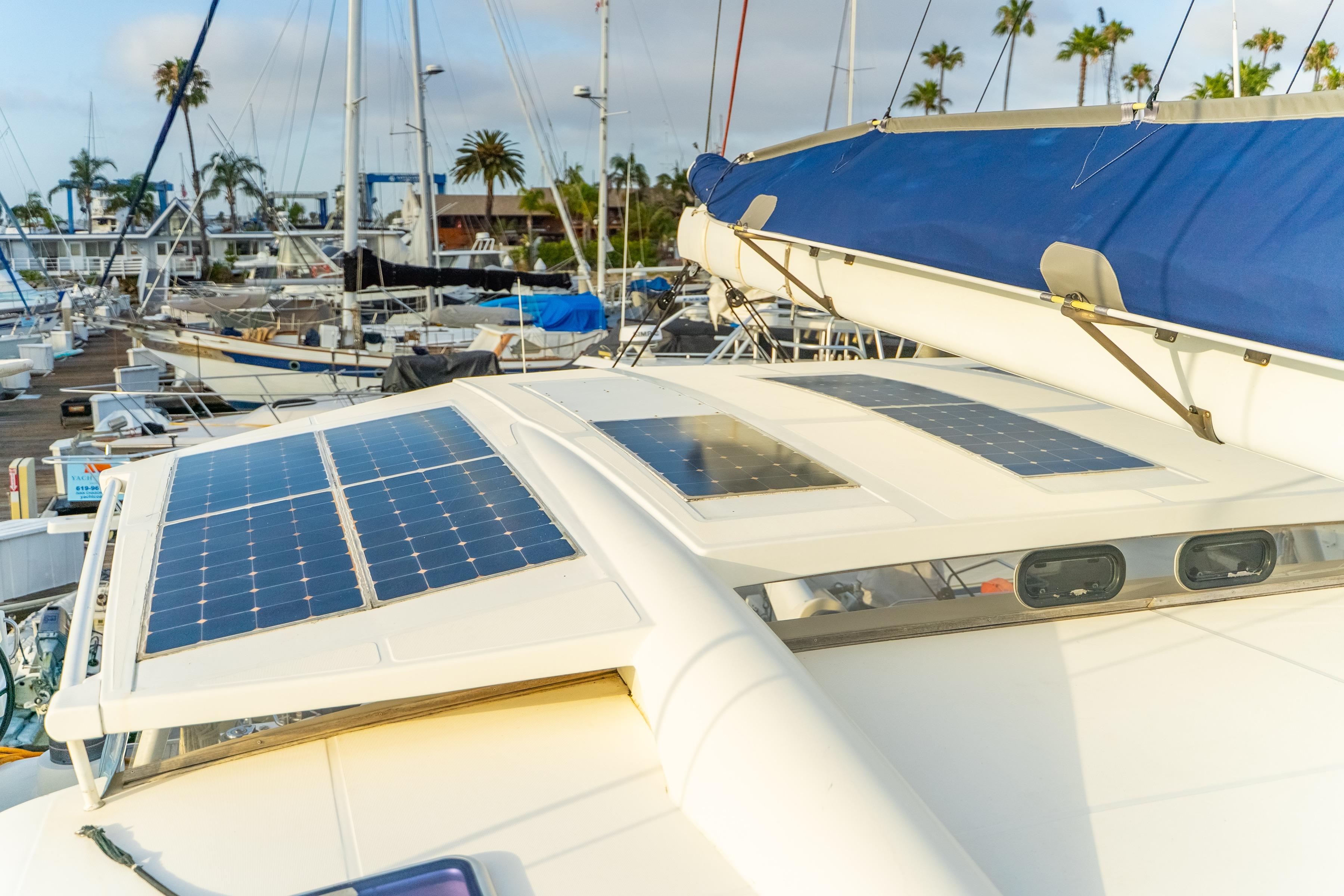 Catana 65 catamaran (2009) with solar panels docked at a marina, surrounded by palm trees.
