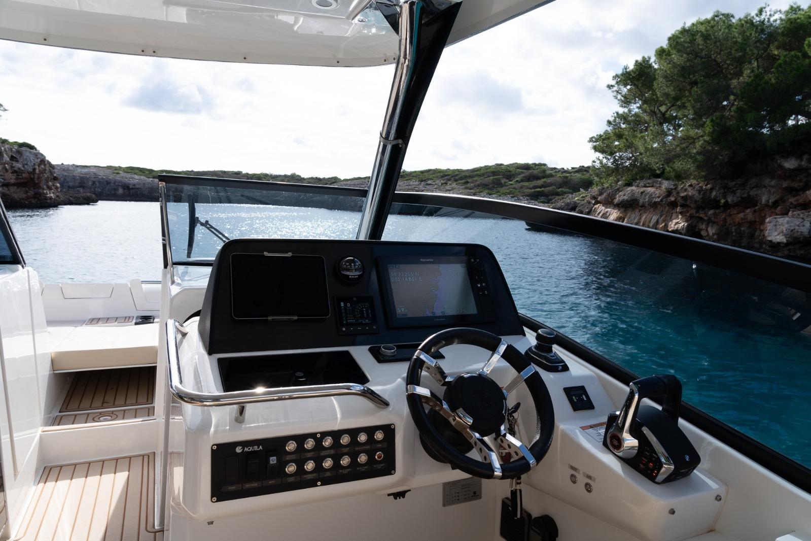 Cockpit view of 2023 Aquila 32 yacht, featuring modern controls and scenic waterway backdrop.