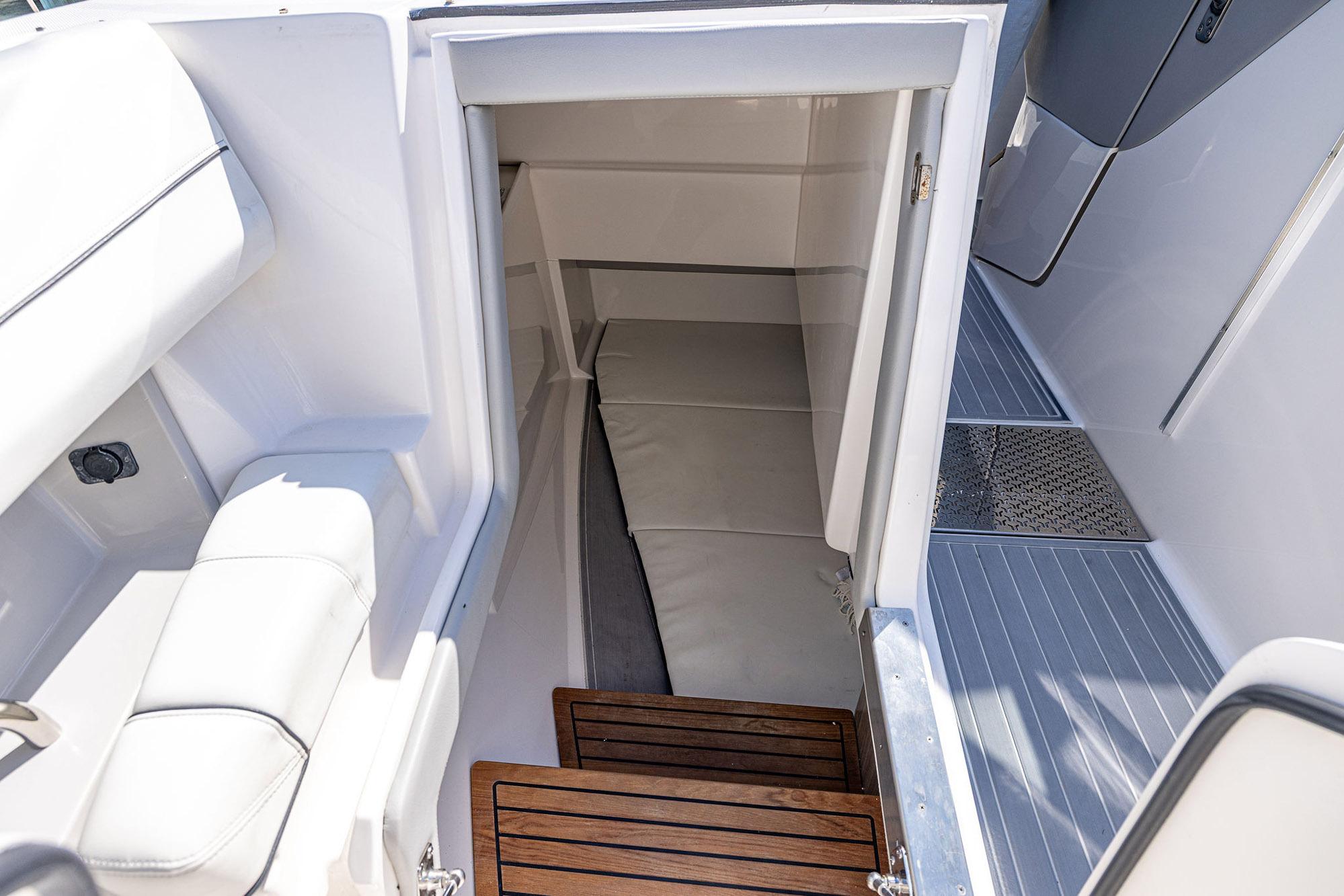 Interior cabin view of 2022 Regal LX36 boat, featuring sleek white seating and wooden steps.