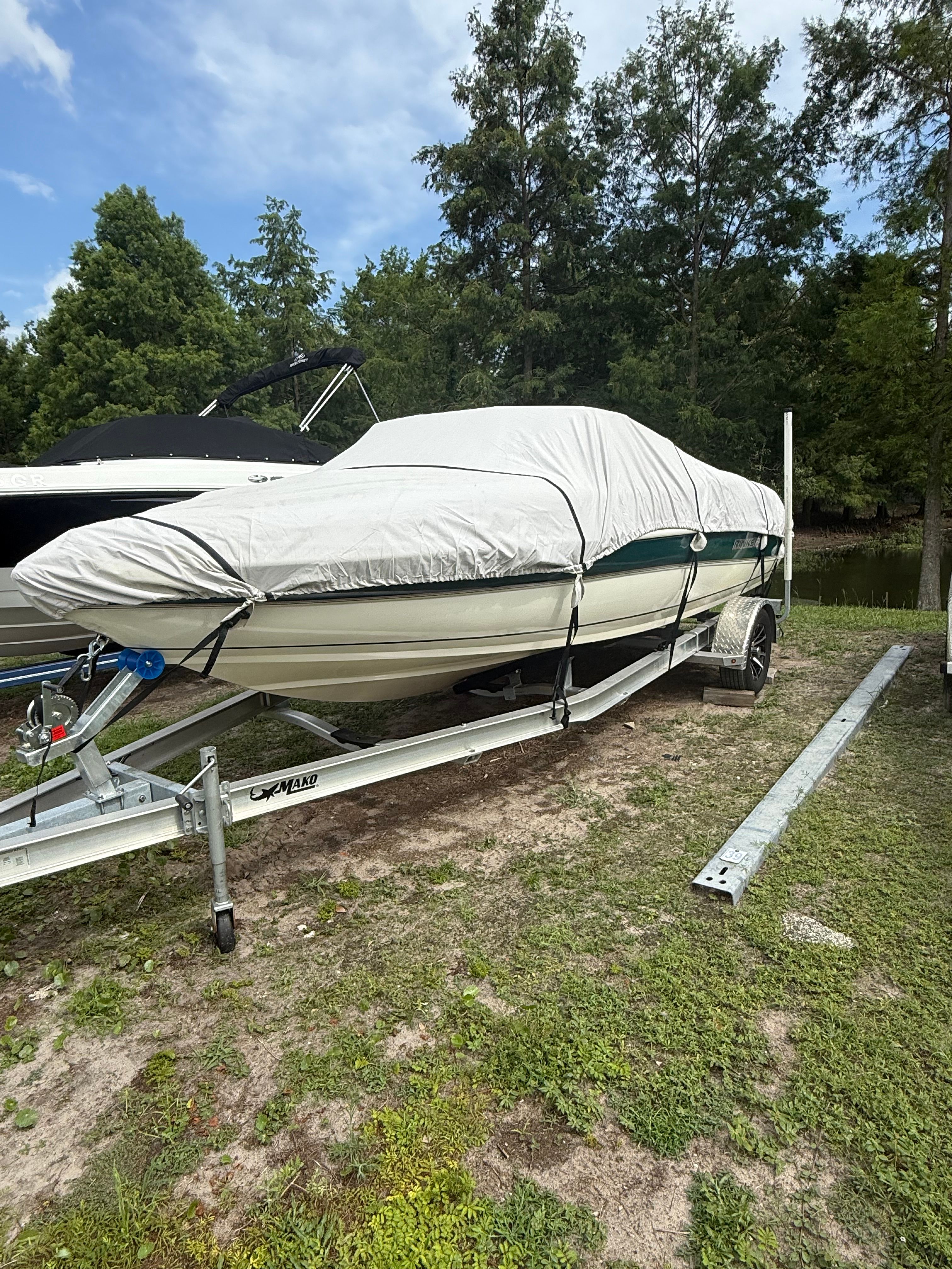 A covered boat on a trailer, surrounded by trees and grass.