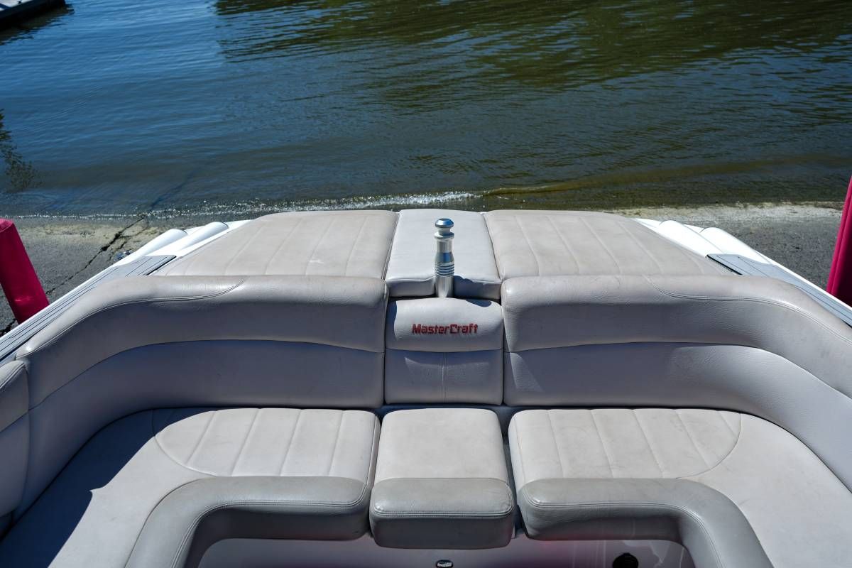Rear view of a MasterCraft X-45 boat with gray upholstery by the water.