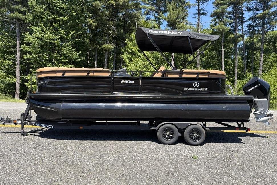 2026 Regency 230 DL pontoon boat on trailer, parked outdoors with forest background.