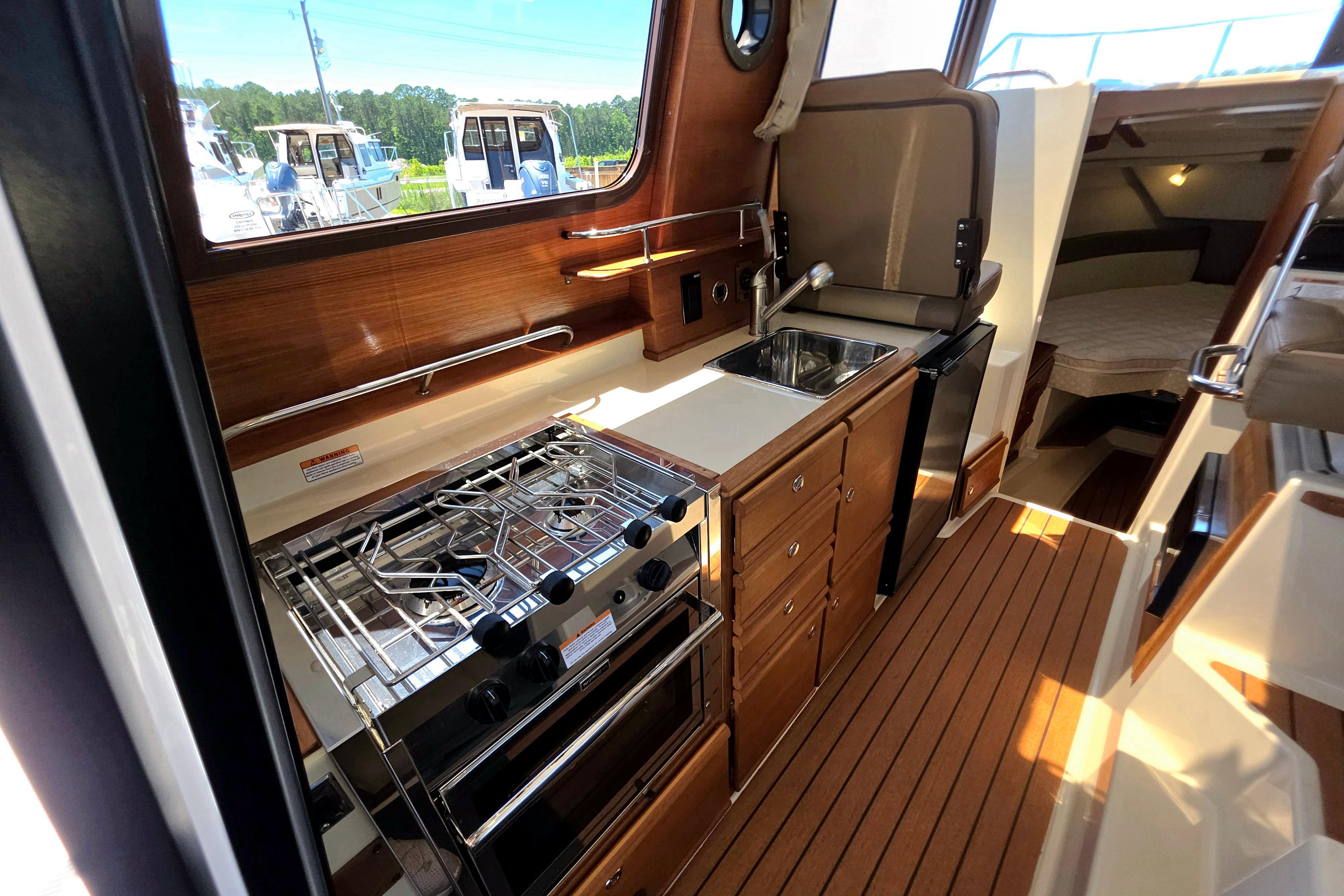 2021 Ranger Tug R27 interior kitchen with stove, sink, and wooden cabinetry.