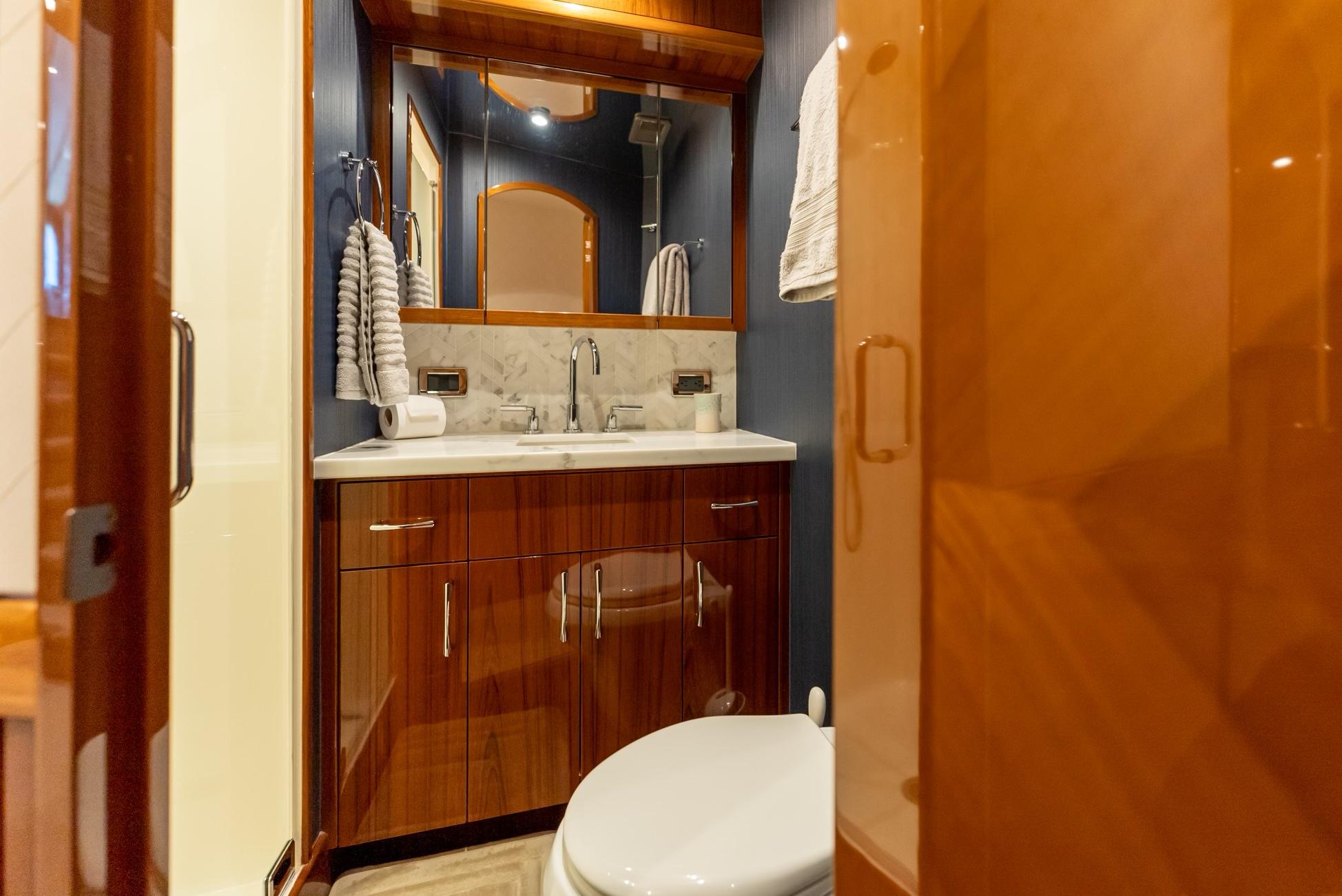 Luxurious bathroom in 2018 Hatteras GT70 yacht with wooden cabinetry and marble countertop.