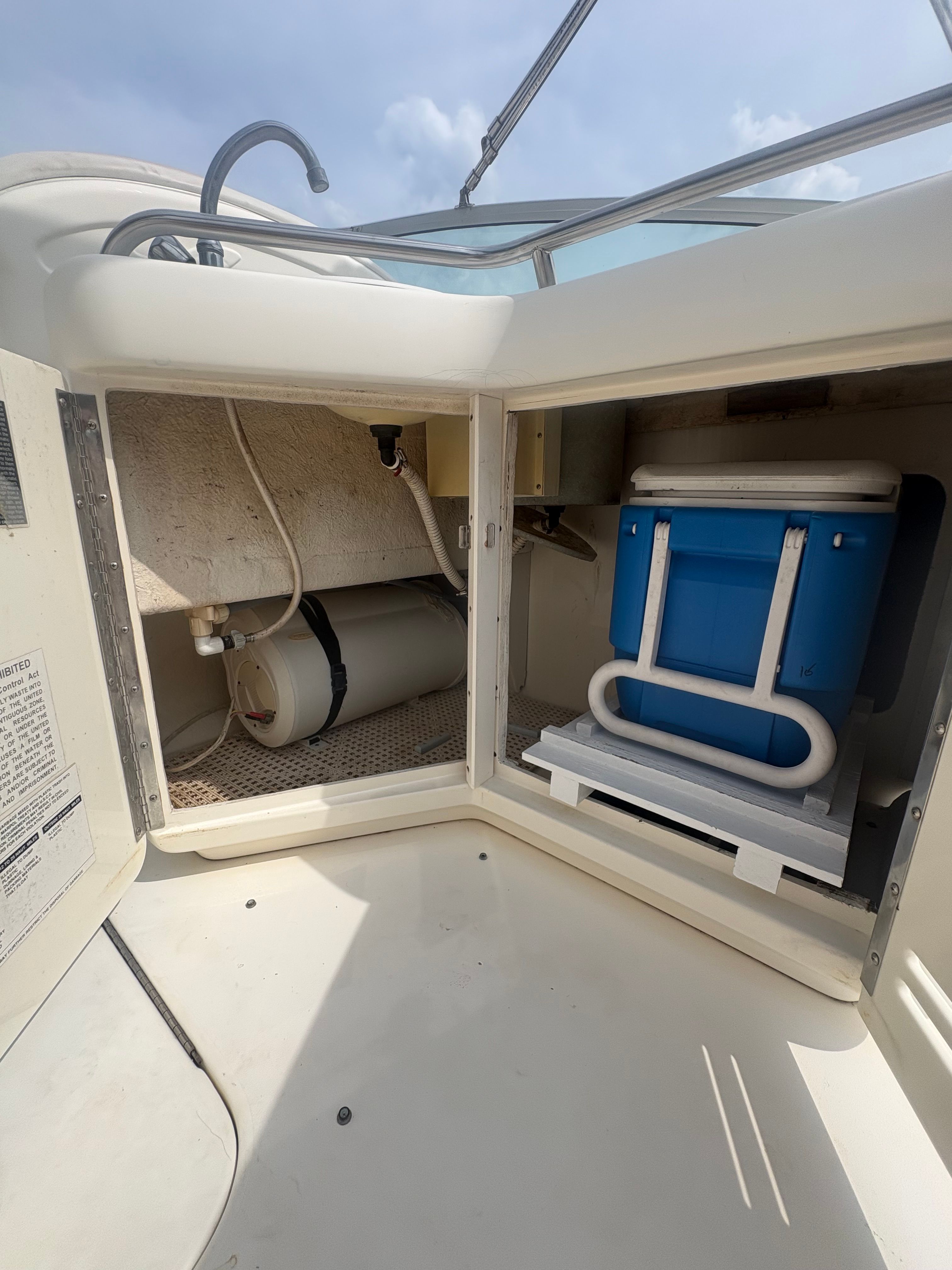 An open storage compartment on a boat reveals a blue cooler and a water tank.