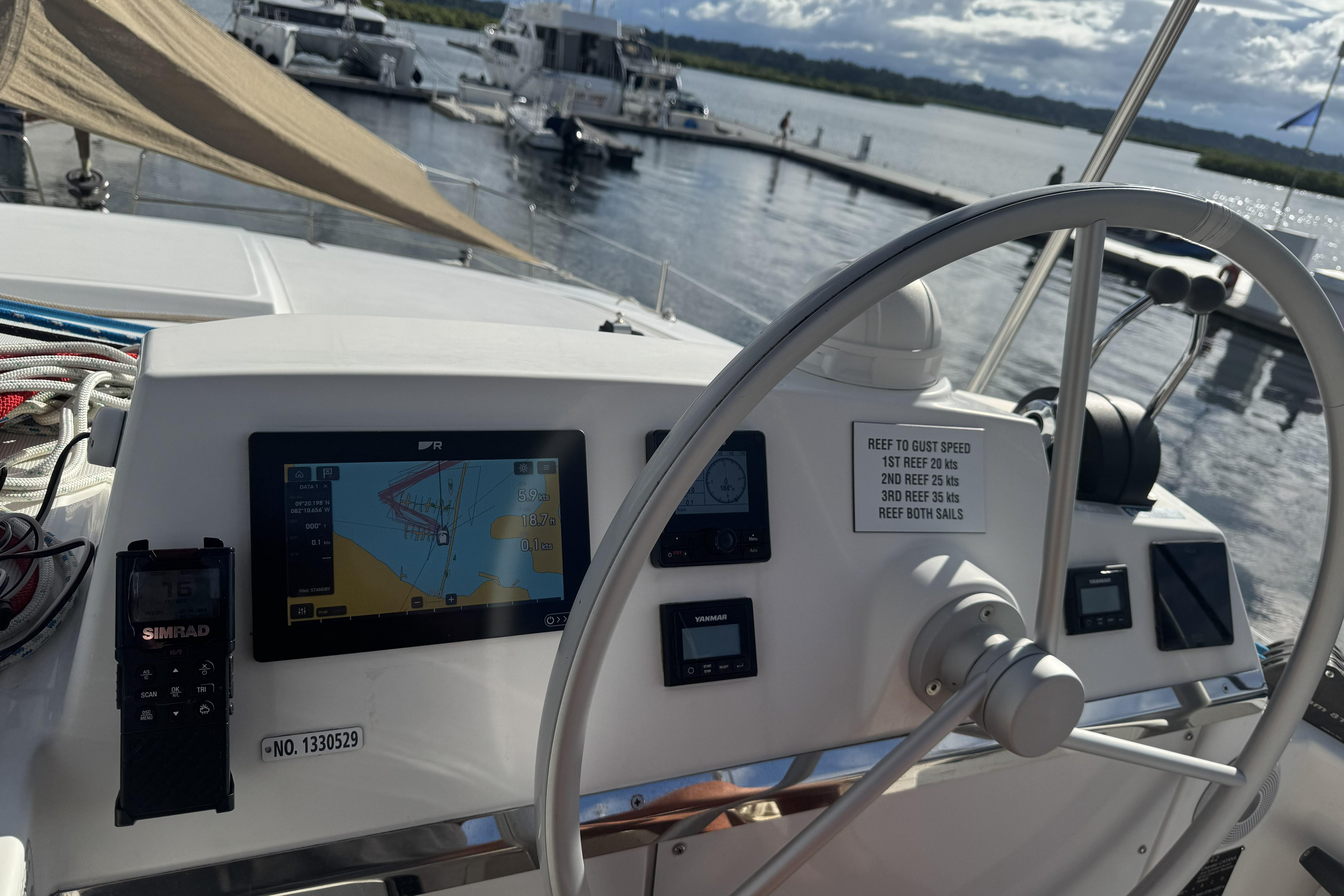 Helm of 2023 Bali 4.2 catamaran with navigation equipment and steering wheel, docked at marina.