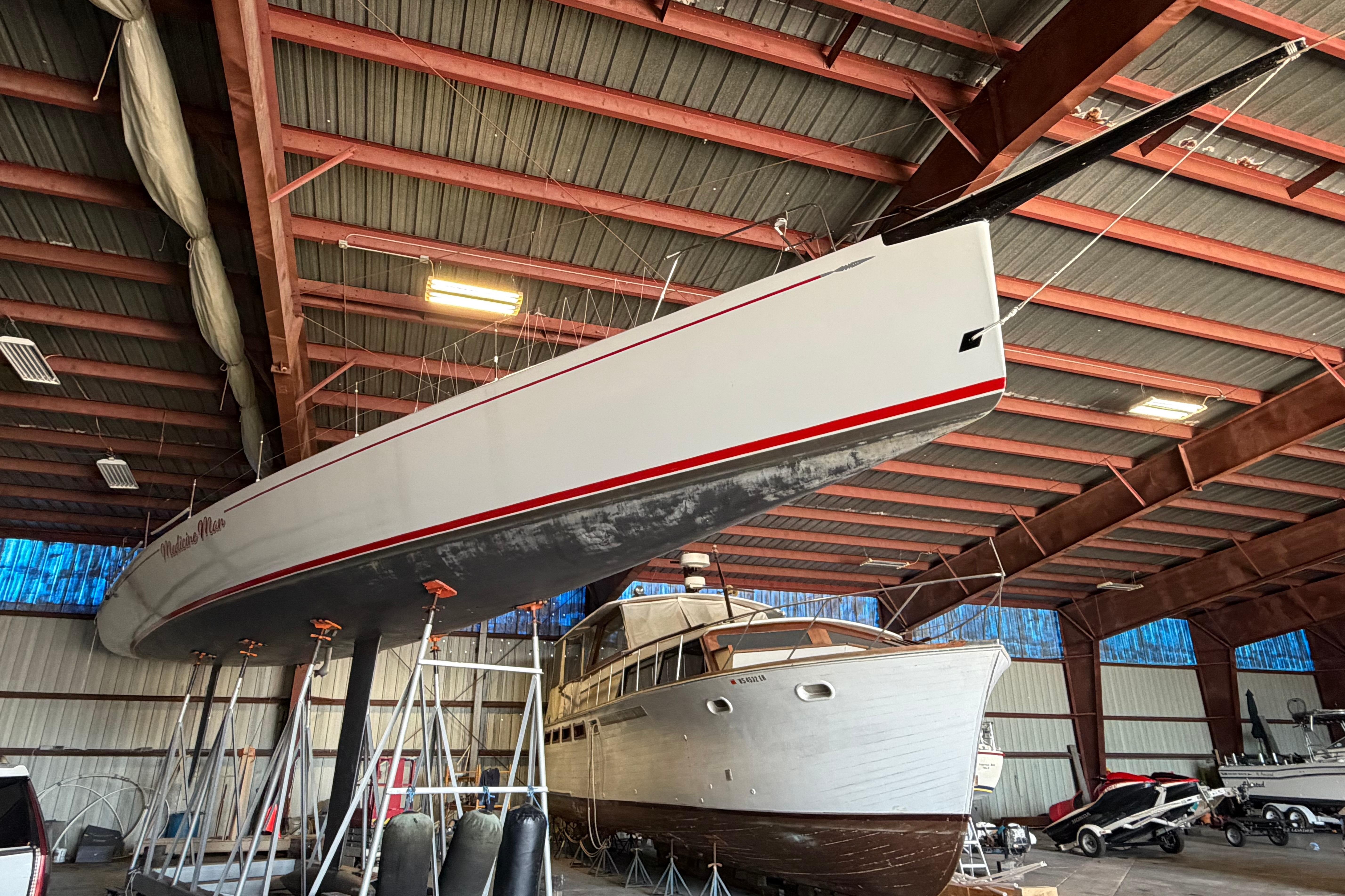Andrews 63 sailboat in a warehouse, elevated on stands, alongside a wooden yacht.