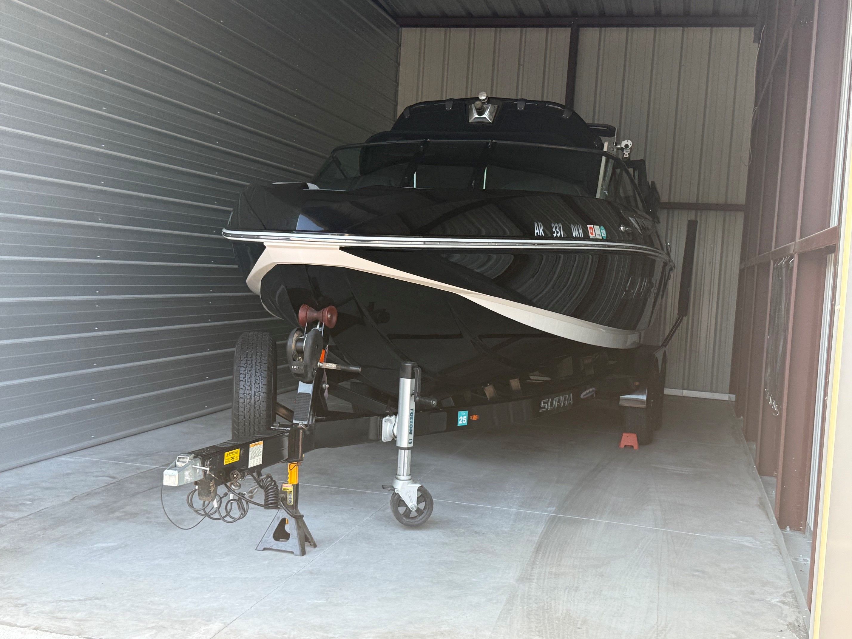A black boat on a trailer inside a warehouse.