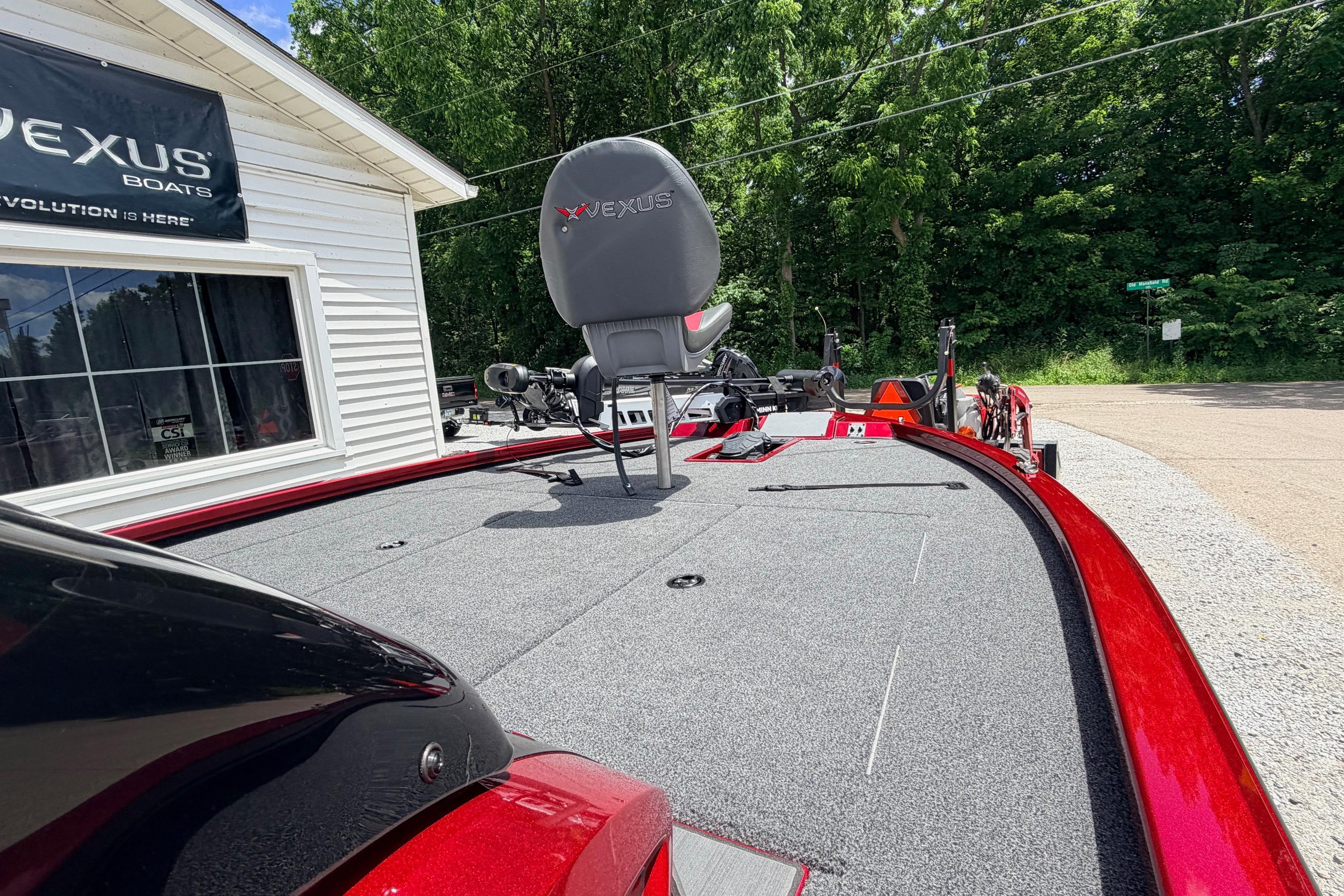 2026 Vexus AVX1985s boat with red accents, parked outside dealership, surrounded by trees.