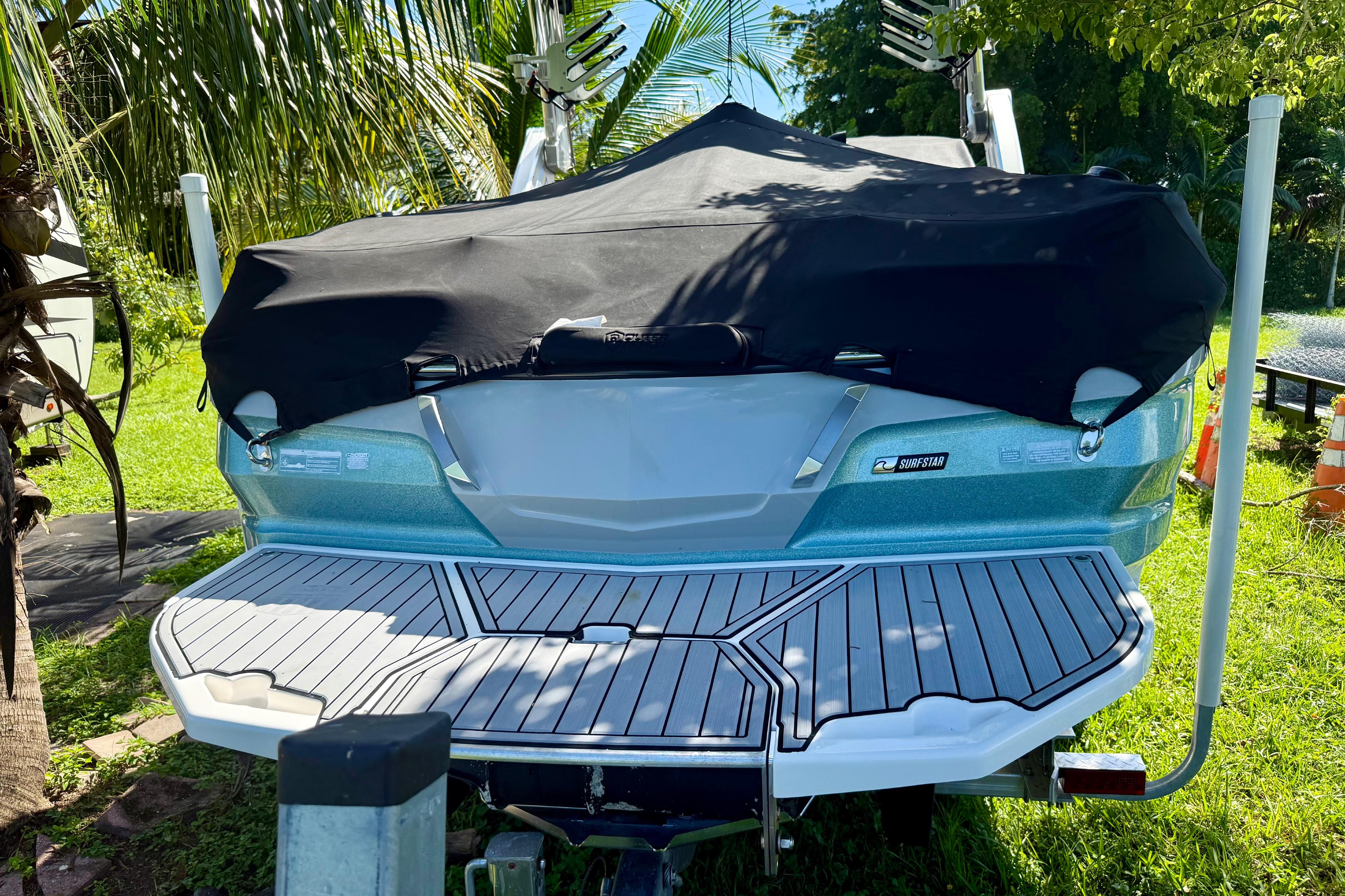2023 MasterCraft X24 boat with cover, parked outdoors, surrounded by lush greenery.