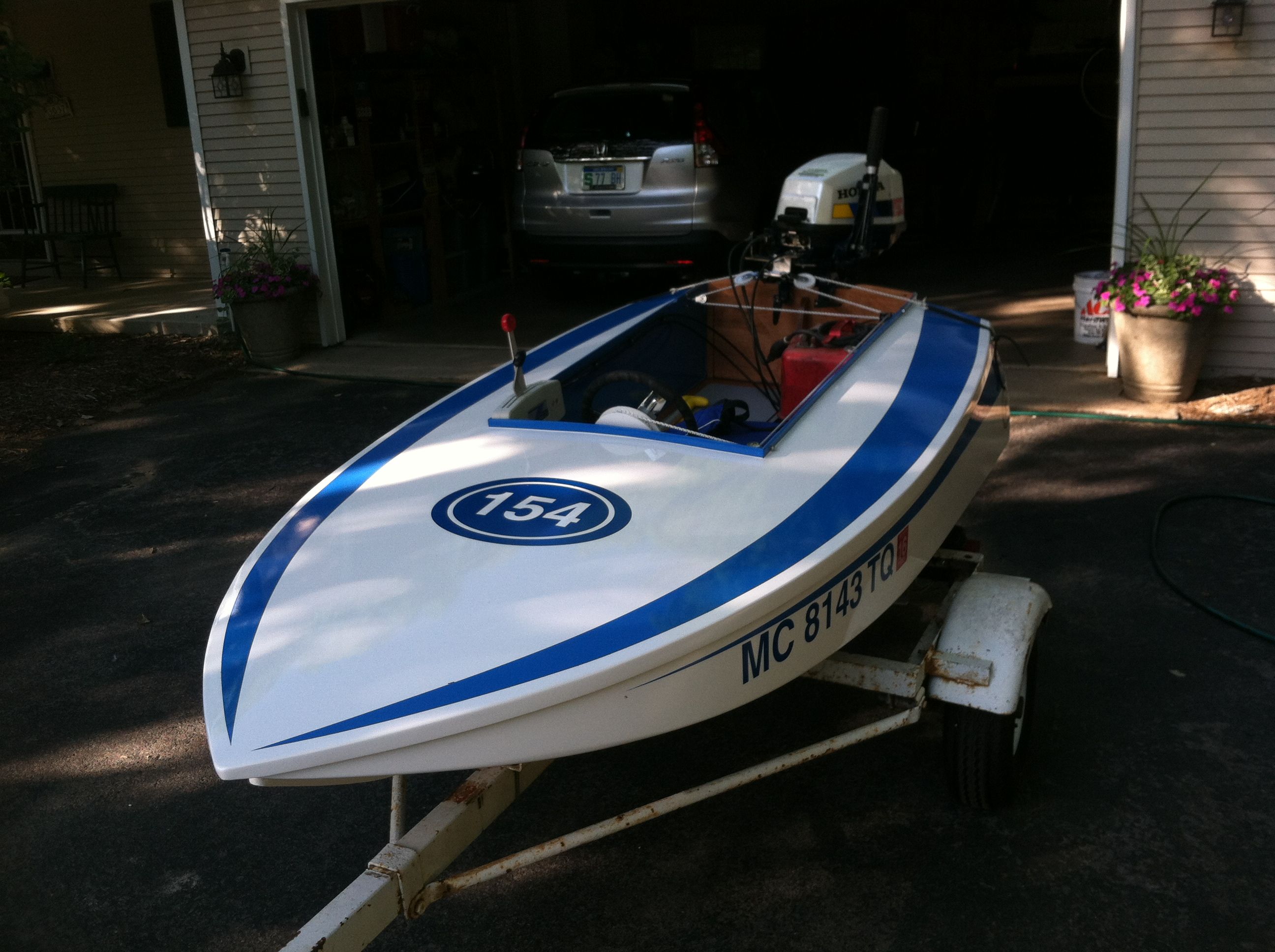 A white and blue racing boat on a trailer in front of a garage.